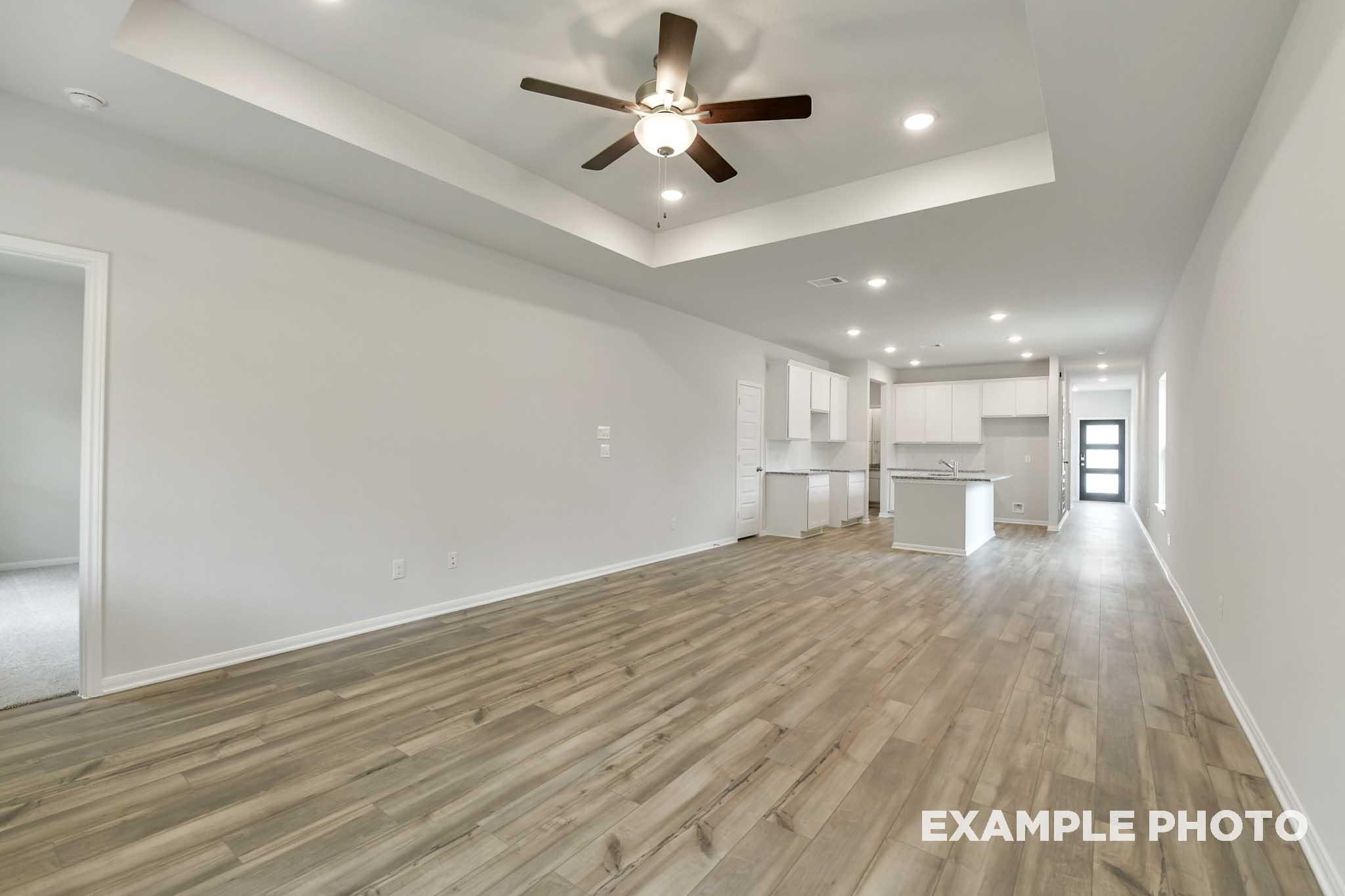 Open-concept living room and kitchen in The Frio floor plan featuring a tray ceiling, wood-look flooring, and white cabinets.