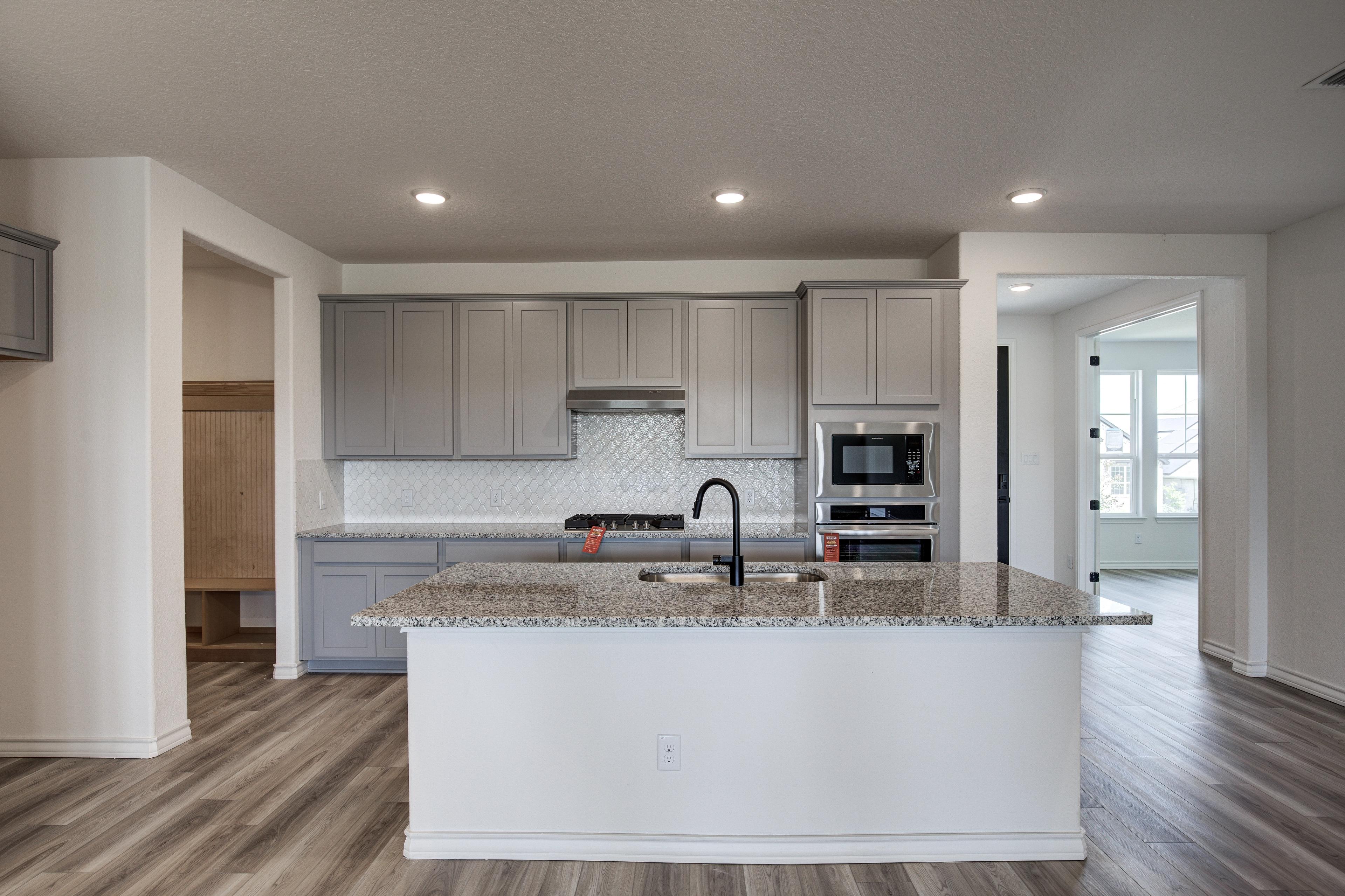 Spacious modern kitchen in The Lanier by Davidson Homes featuring gray shaker cabinets, large white quartz island, and stainless steel appliances