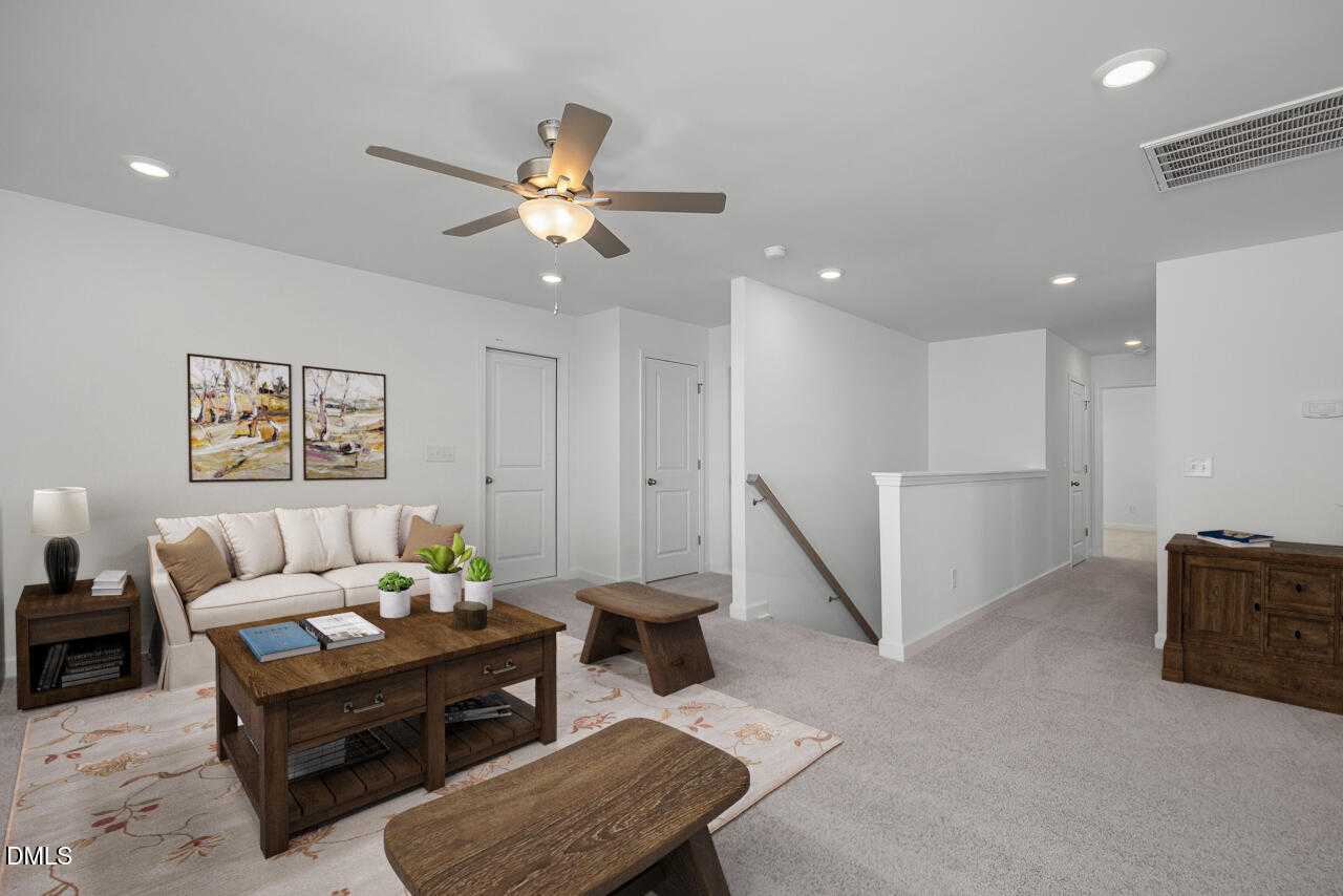 Cozy upstairs loft with white sofa, wooden coffee table, ceiling fan, and neutral decor in The Cypress B II home, Angier, NC
