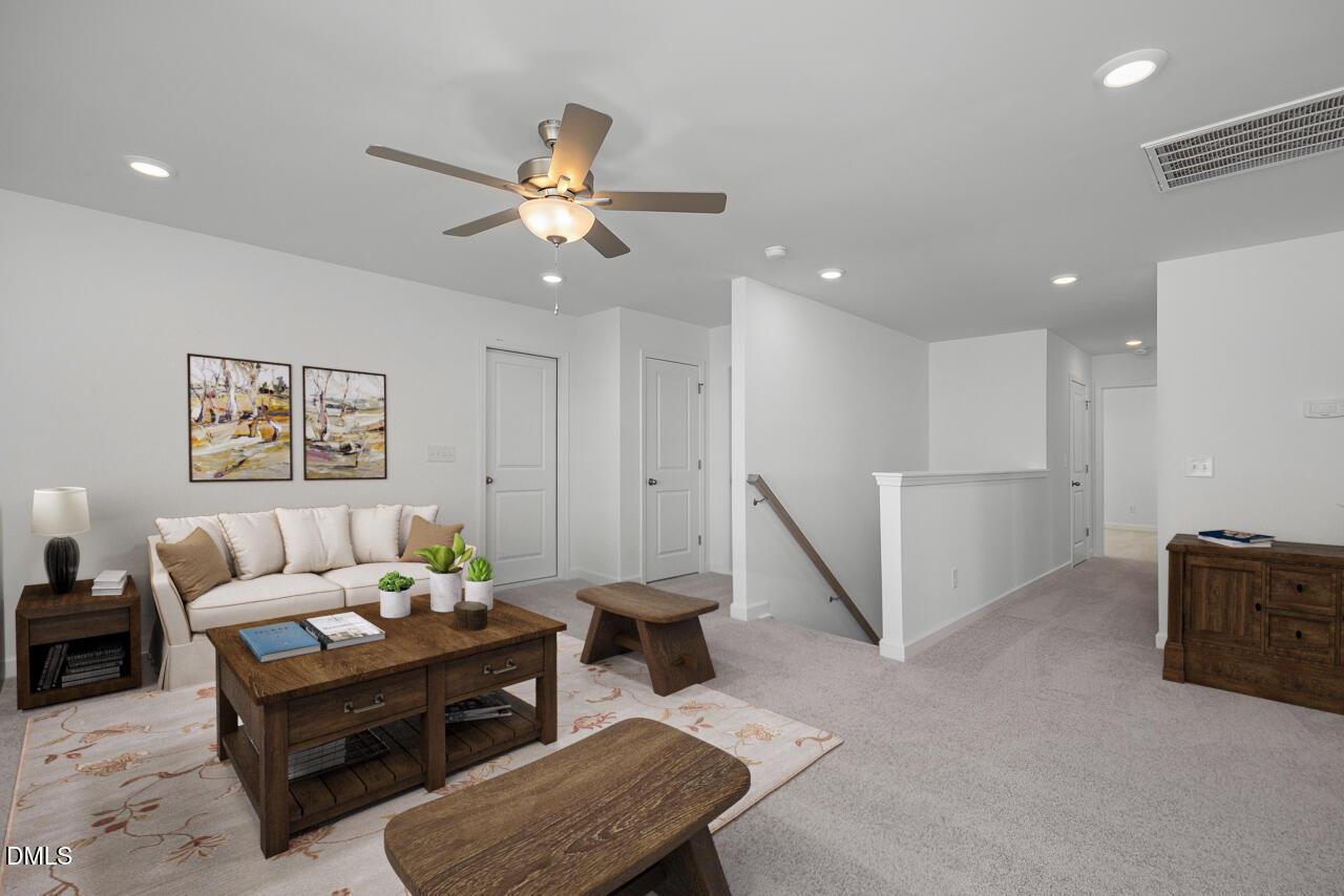Cozy upstairs loft with white sofa, wooden coffee table, plants, and ceiling fan in The Cypress B II by Davidson Homes, Angier, NC