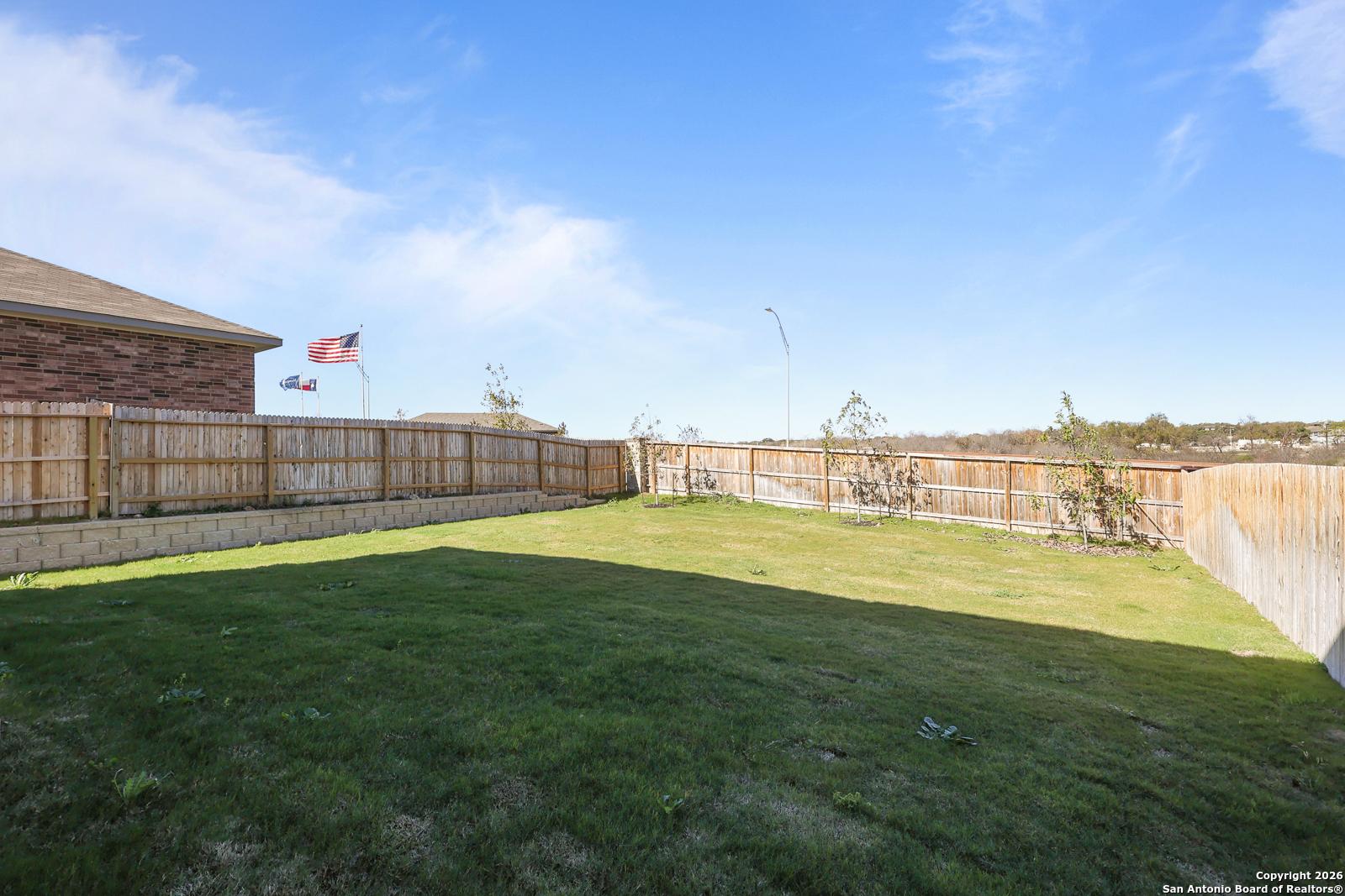 Private fenced backyard with lush green lawn, brick home exterior, and American flag in Davidson Homes The Murray K, Comanche Ridge, San Antonio, Texas