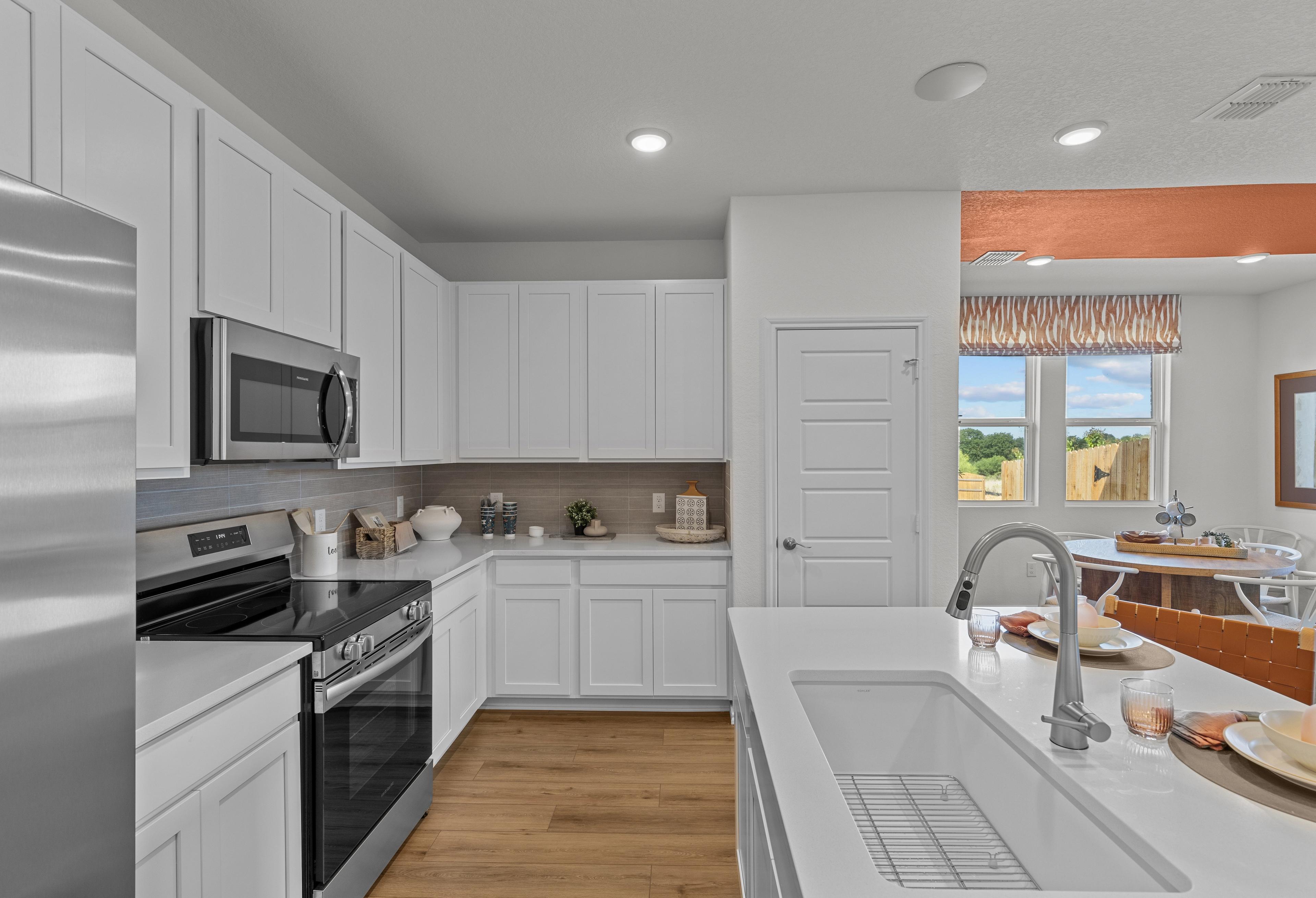 Spacious kitchen in The Daphne I with white shaker cabinets, stainless steel appliances, large island sink, and open dining nook
