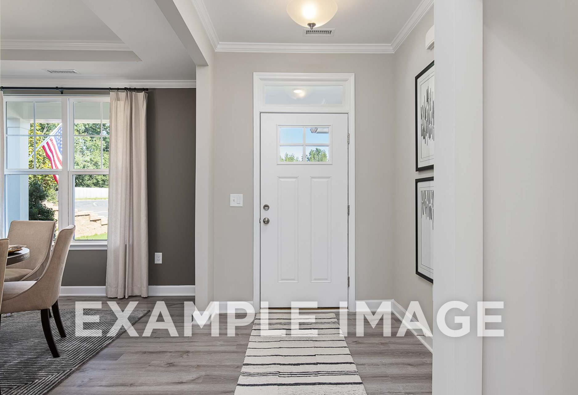 Inviting foyer of The Ash D with white front door, open dining area, hardwood floors, and window views in Davidson Homes design, Angier NC