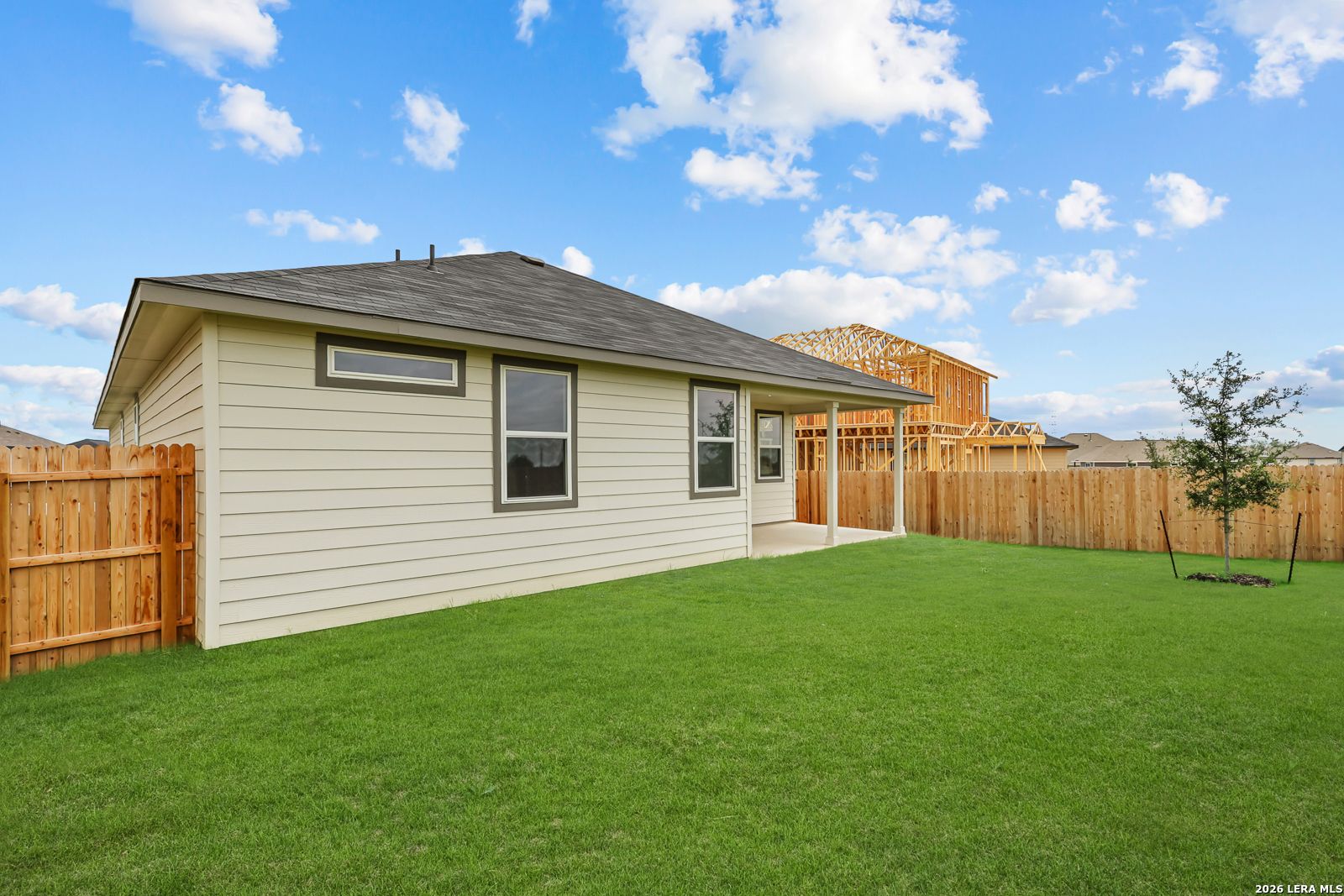 Beige single-story home with covered porch, wooden fence, and green yard in Hickory Ridge, Elmendorf, Texas - Davidson Homes The Glenwood E