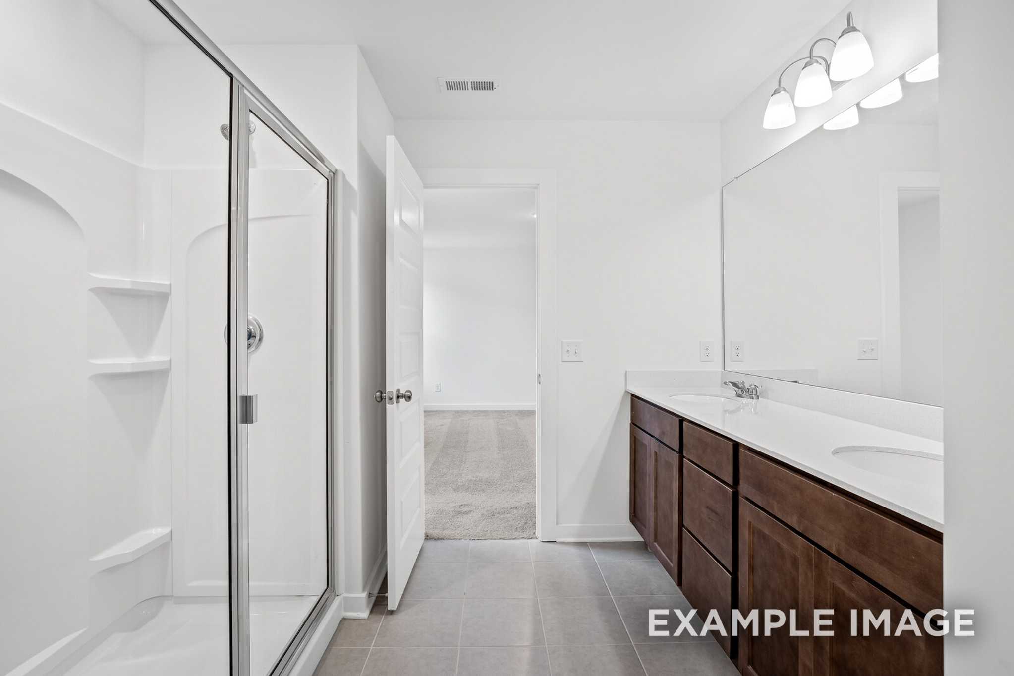 Spacious master bathroom in The Grayson C featuring glass shower enclosure, double vanity with shaker cabinets, and sleek lighting