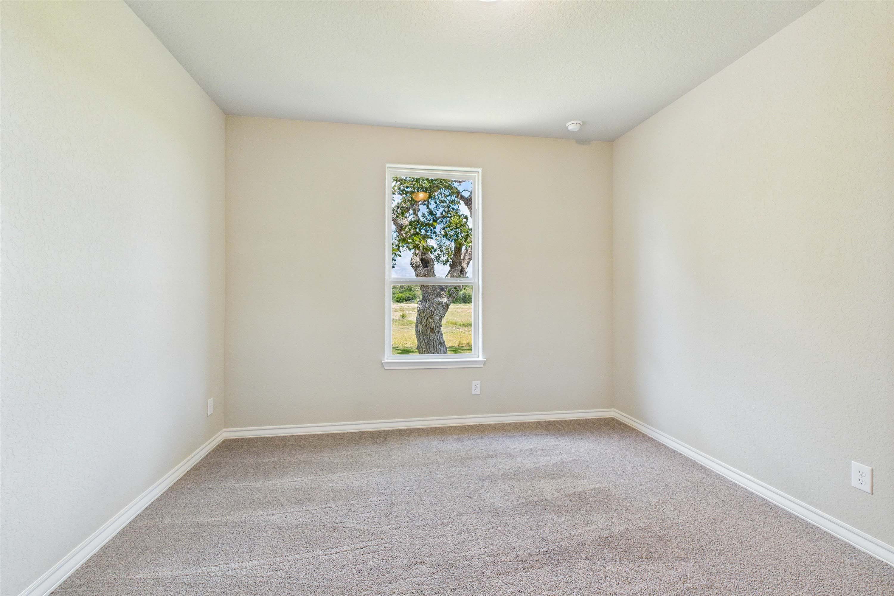 Spacious bedroom in The Foster home design featuring neutral walls, plush carpeting, and a view of trees from the window.