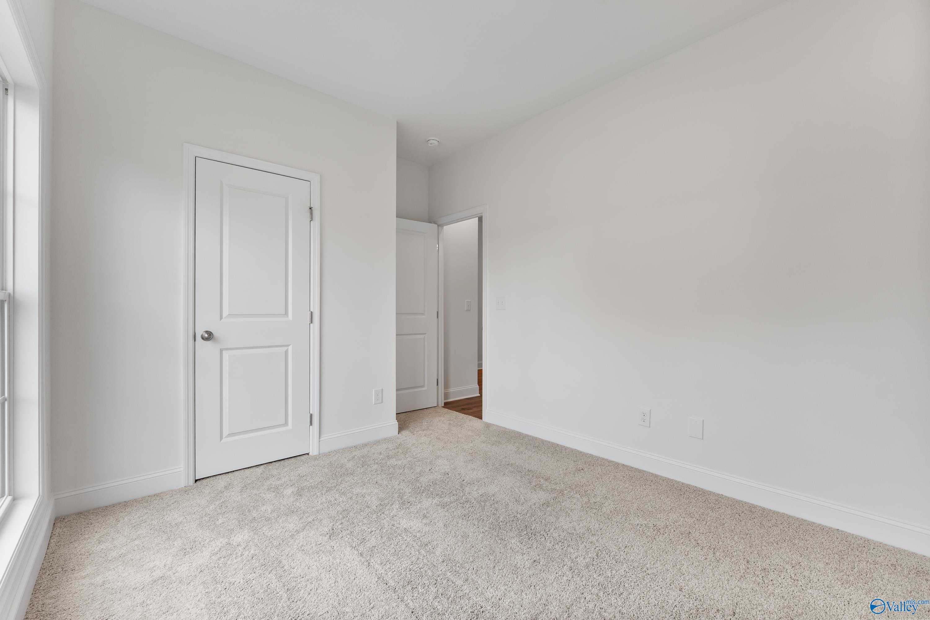 Spacious empty bedroom with white walls, beige carpet, double doors, and large window in Davidson Homes Asheville C, New Market, AL