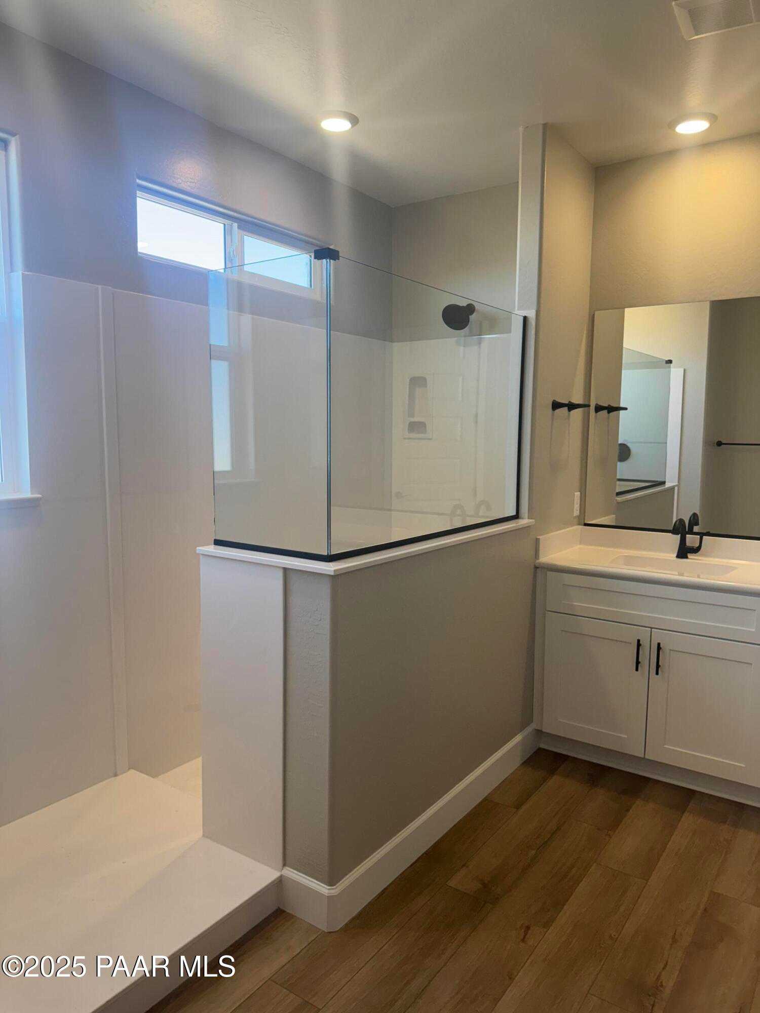 Modern master bathroom with frameless glass shower, single vanity sink, and wood flooring in Evermore Homes The Summit B, Prescott Valley, AZ
