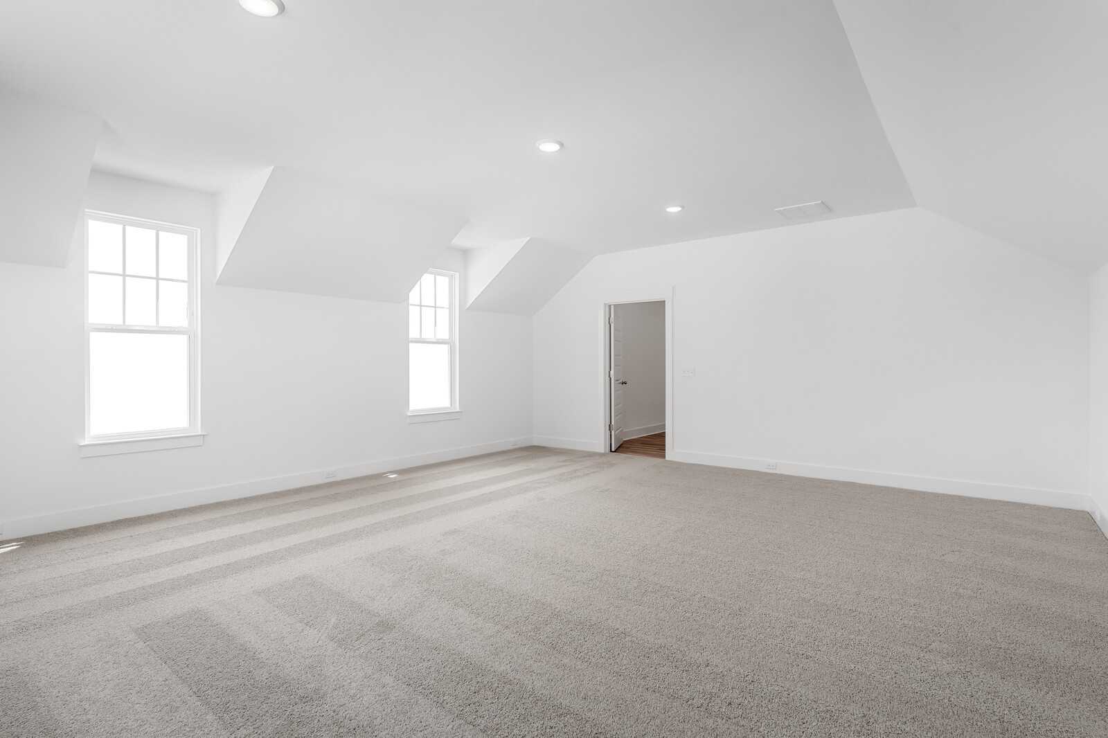 Bright upstairs bedroom with vaulted ceiling, dormer windows, white walls, and carpeted floor in Davidson Homes The Hathaway, Murfreesboro, TN