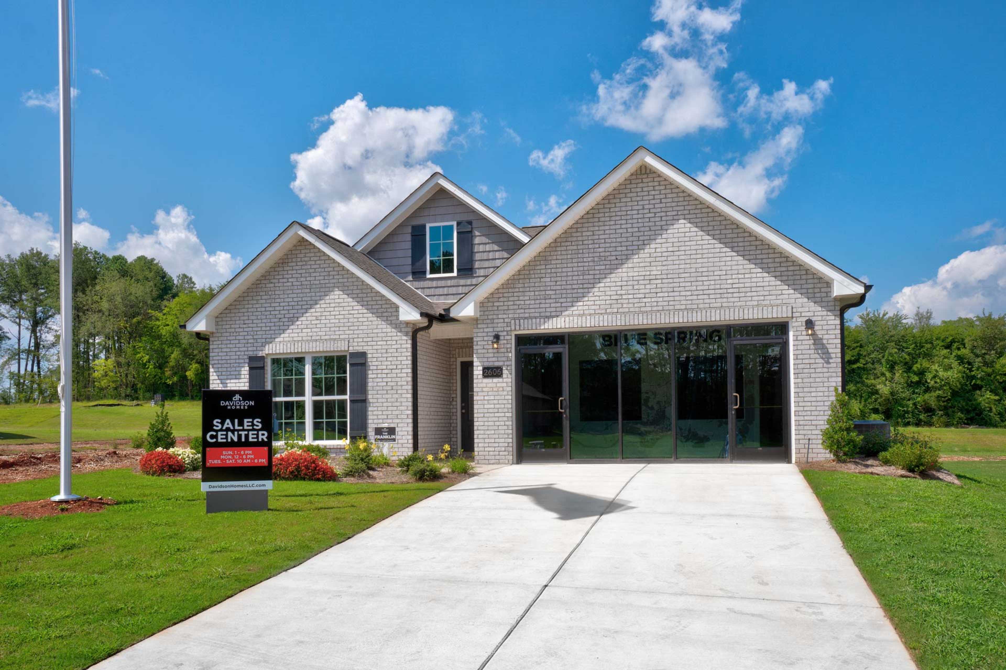 Brick new home exterior at Blue Spring in Huntsville Alabama with garage driveway and sales center sign