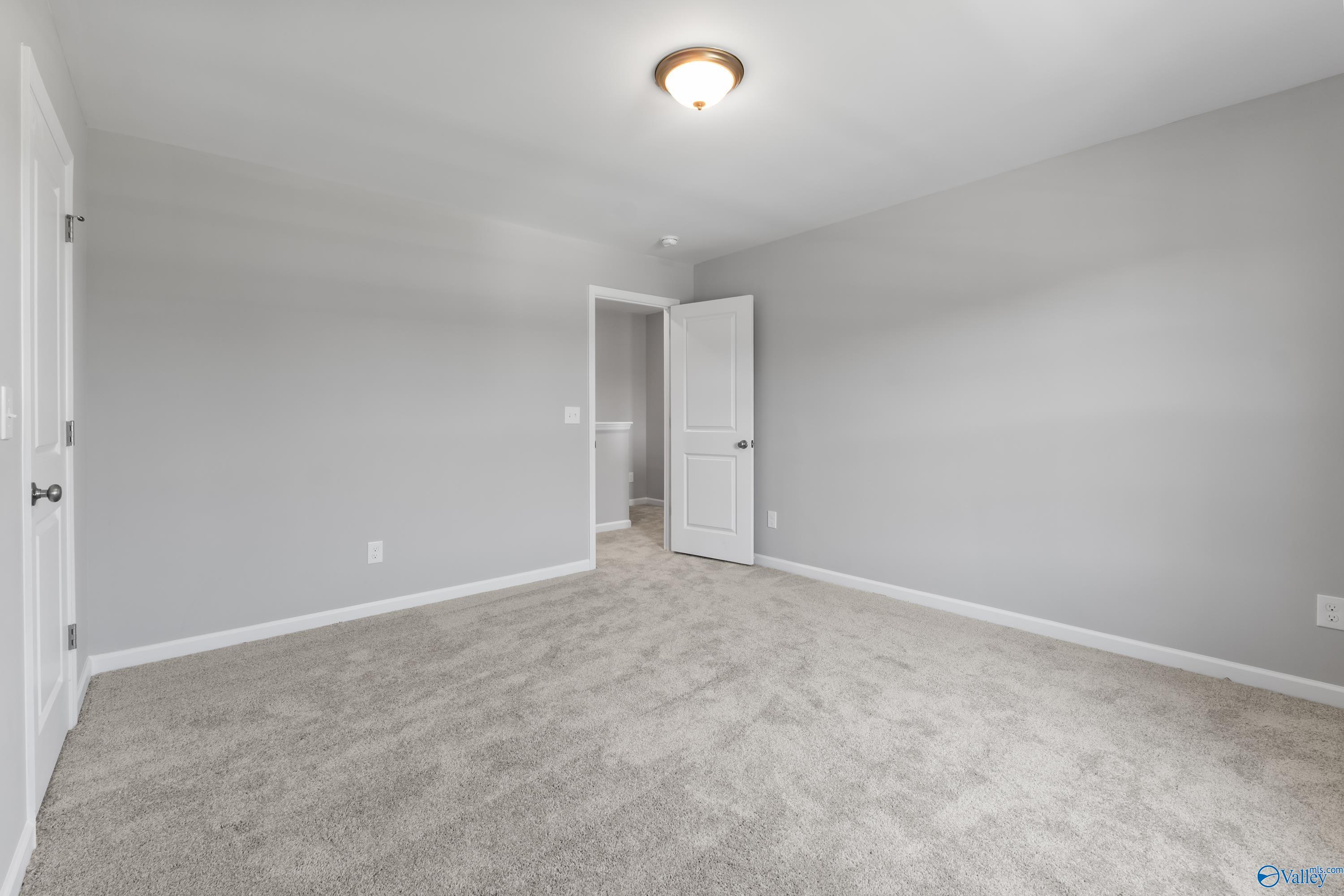 Spacious empty bedroom with gray walls, beige carpet, and en-suite bath door in Davidson Homes The Charm, Huntsville AL