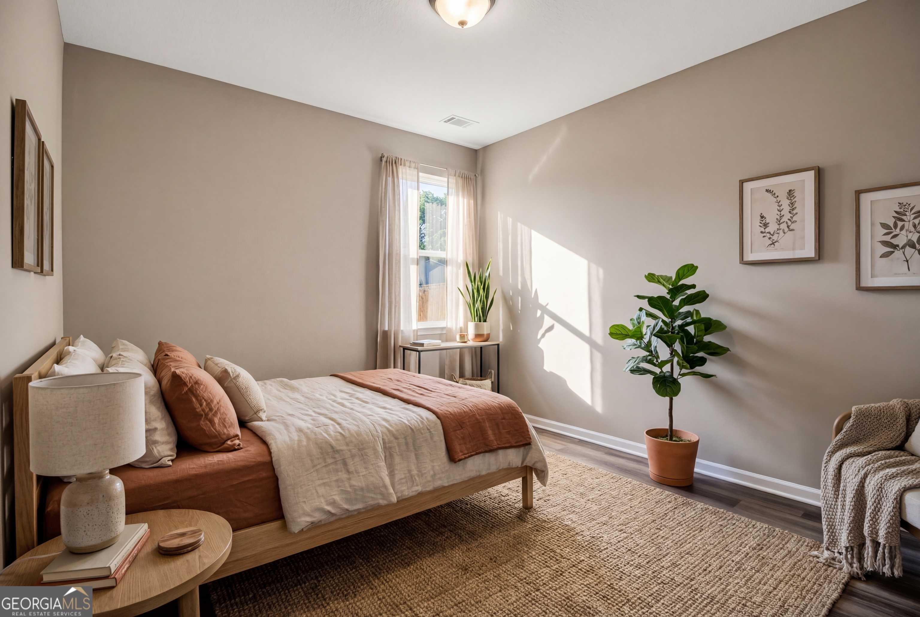 Cozy beige bedroom with wooden bed, terracotta accents, potted plants, and botanical art in Evermore Homes The Luna, Perry, Georgia