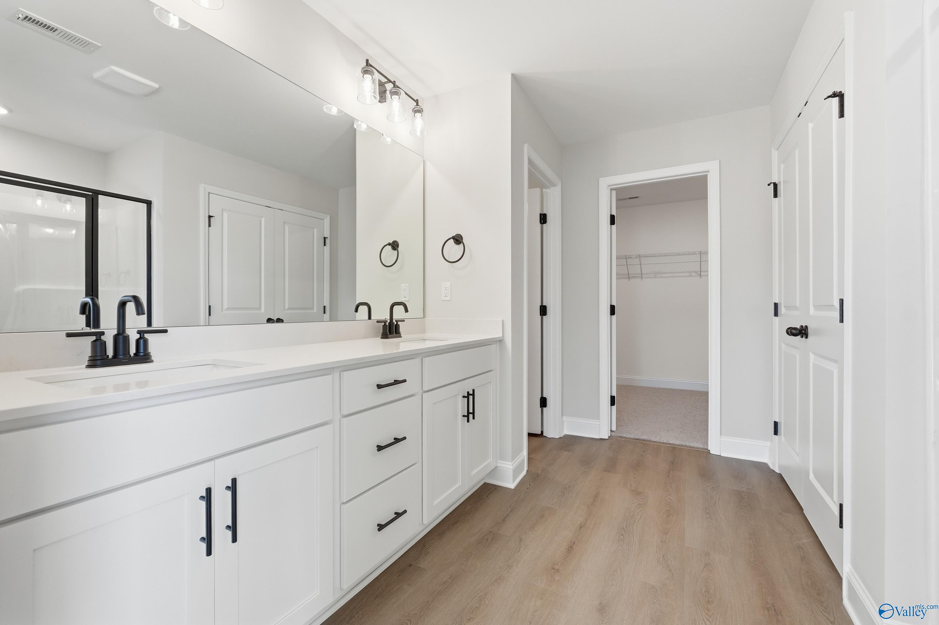 Modern master bathroom featuring double white vanity, quartz countertop, large mirror, and walk-in closet in Davidson Homes The Chelsea C, Harvest, Alabama