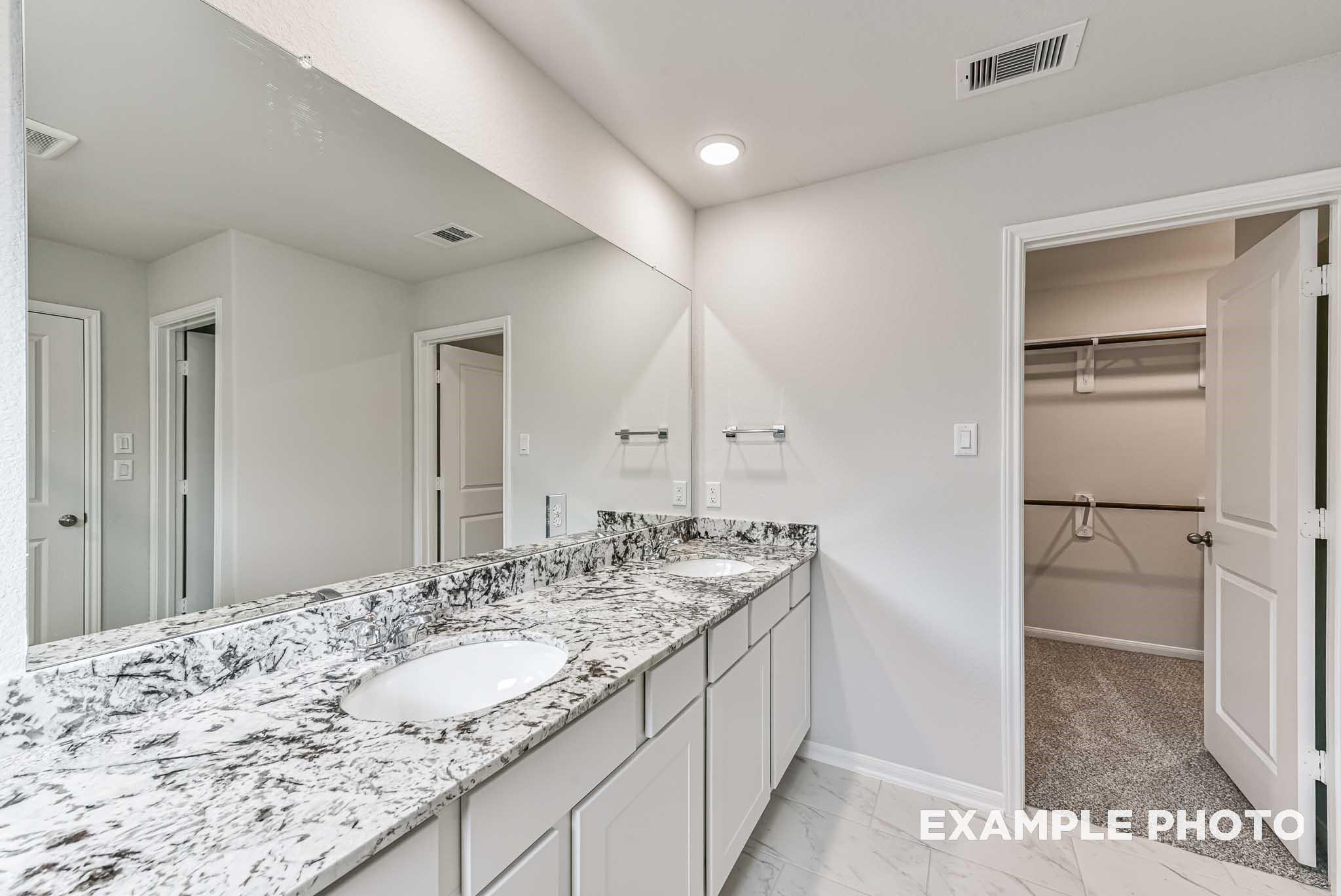 Elegant master bath double vanity with white granite countertop, large mirrors, and open walk-in closet in Davidson Homes The Riviera A, Rosharon, Texas
