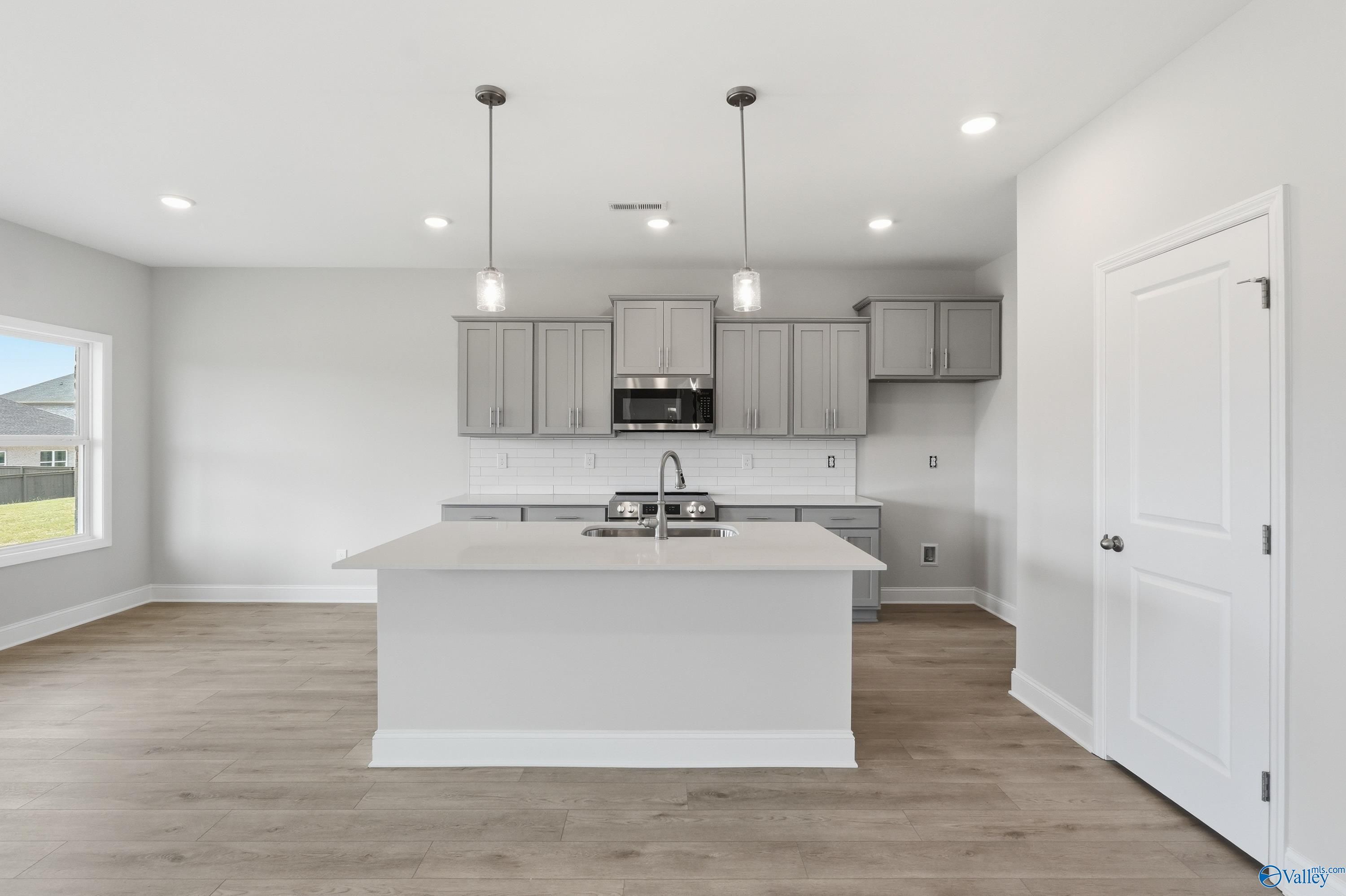 Modern white shaker kitchen with large center island, stainless appliances, pendant lights in The Shelby B home, New Market, Alabama