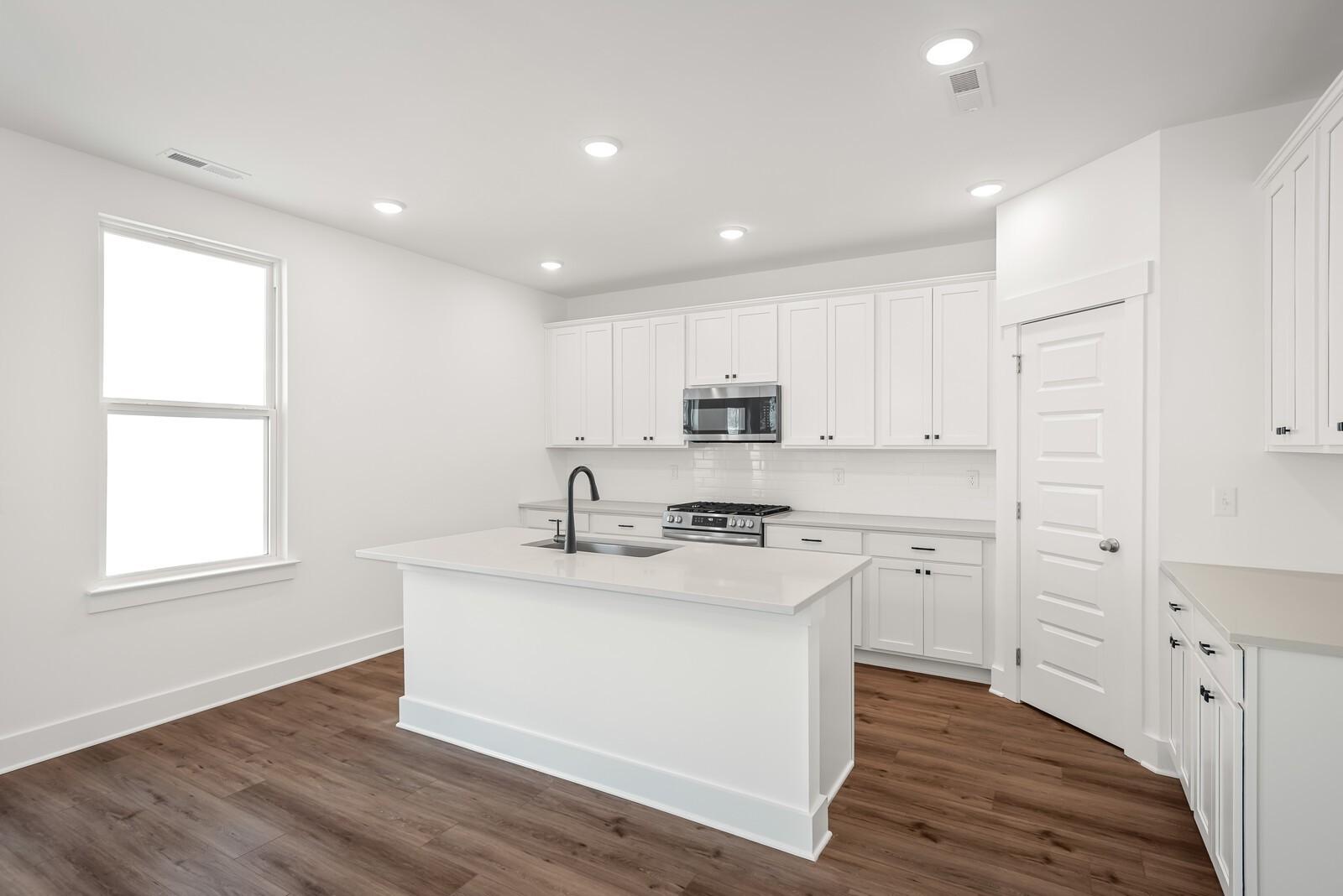 Bright modern kitchen with white cabinets, quartz island sink, and hardwood floors in The Logan C by Davidson Homes, Gallatin