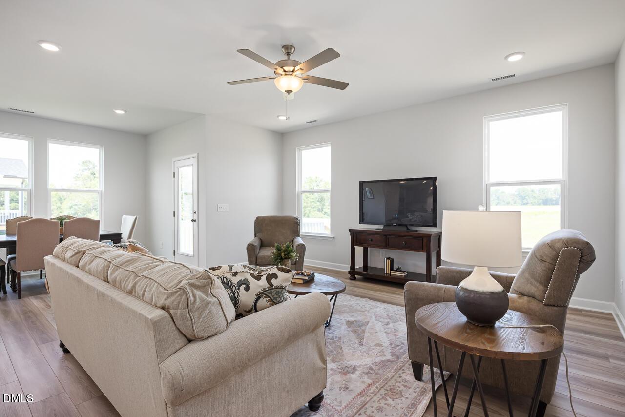 Inviting living room with beige sectional sofa, armchairs, TV console, ceiling fan and large windows in Davidson Homes The Daphne D, Lillington, NC