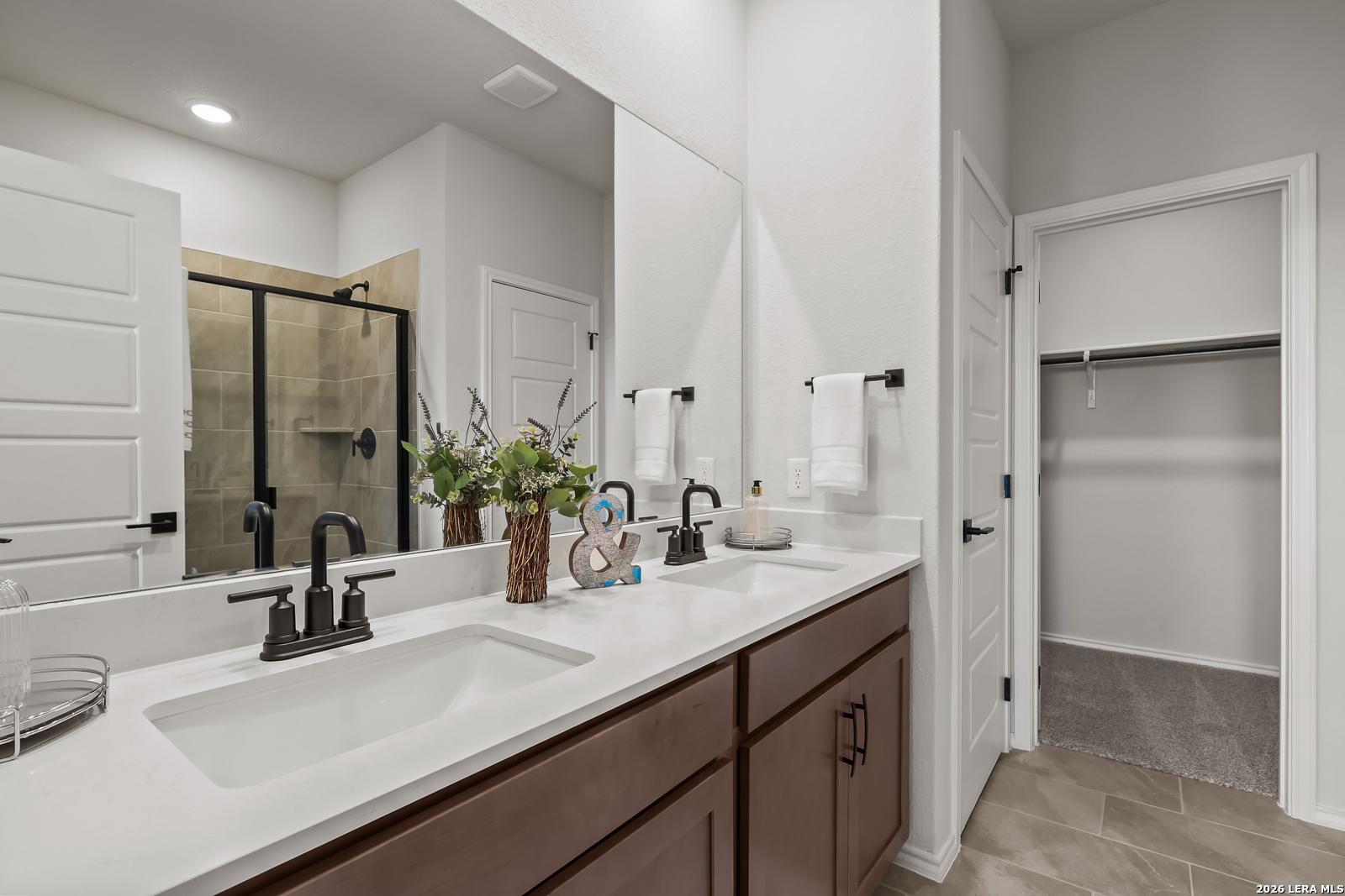 Modern master bathroom featuring double vanity, glass shower, and walk-in closet in Davidson Homes The Daphne H, Seguin, Texas