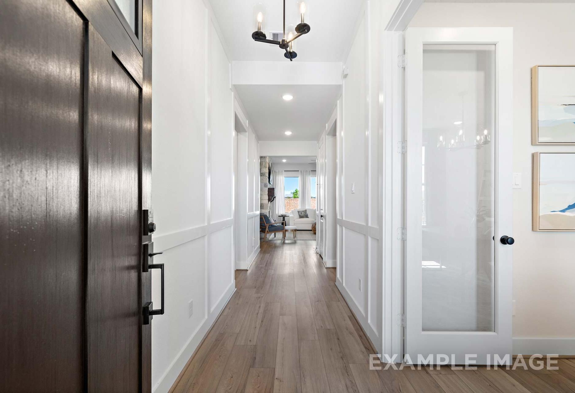 Spacious entry hallway in The Edward A home with hardwood floors, white wainscoting, chandelier, and glass doors