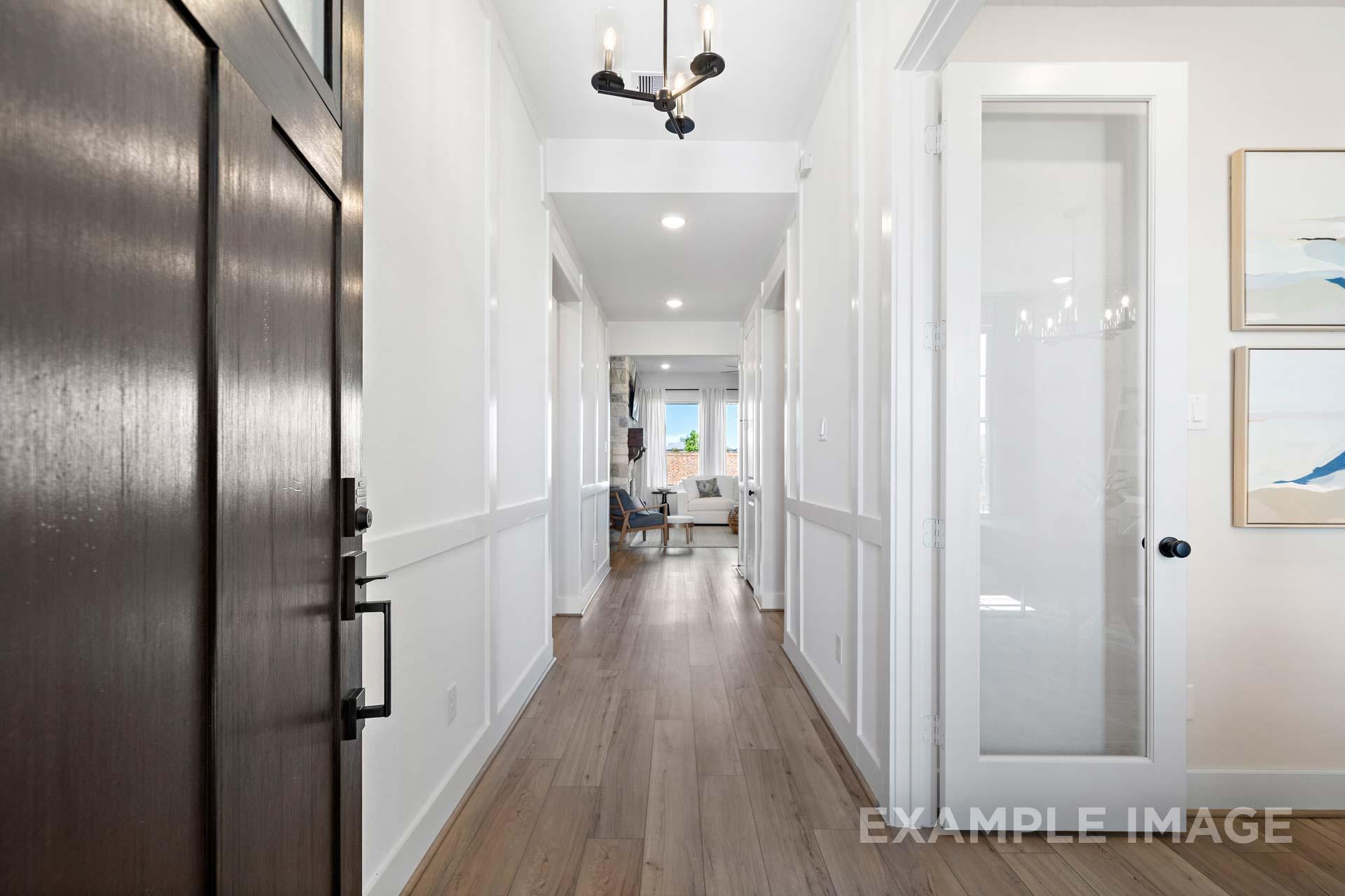 Spacious entry hallway in The Edward C home with open wood door, white wainscoting, hardwood floors, chandelier, and glass doors
