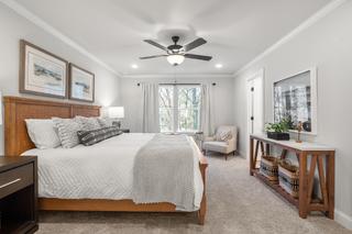 Spacious master bedroom in The Washington H townhome with king bed, wooden headboard, ceiling fan, large window, armchair and plant