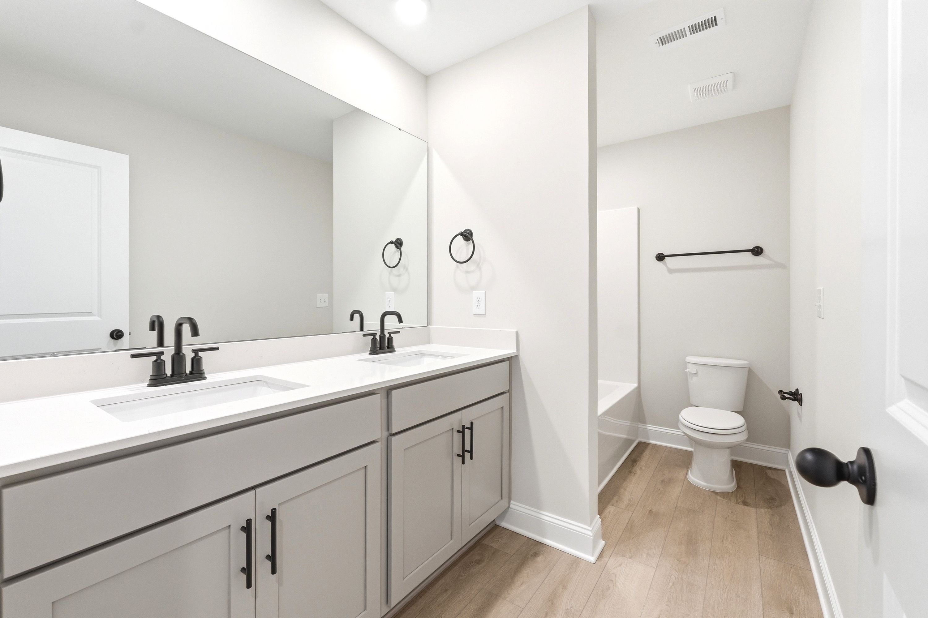 Modern bathroom in The Russell A featuring a dual-sink vanity, matte black fixtures, and wood-look flooring.
