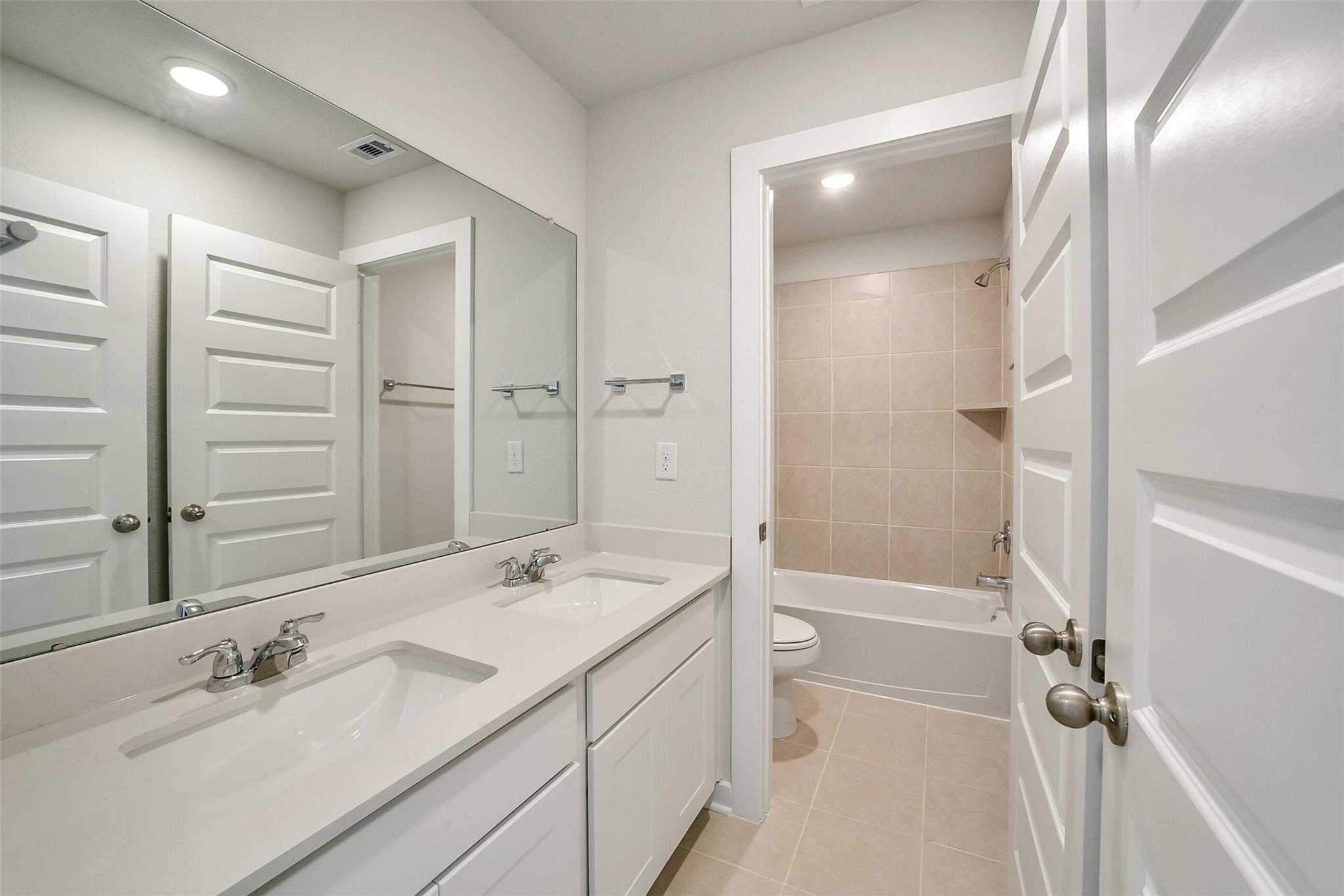 Spacious secondary bathroom with double vanity, bathtub, shower, and white cabinets in Davidson Homes The Blanco E, Magnolia, Texas