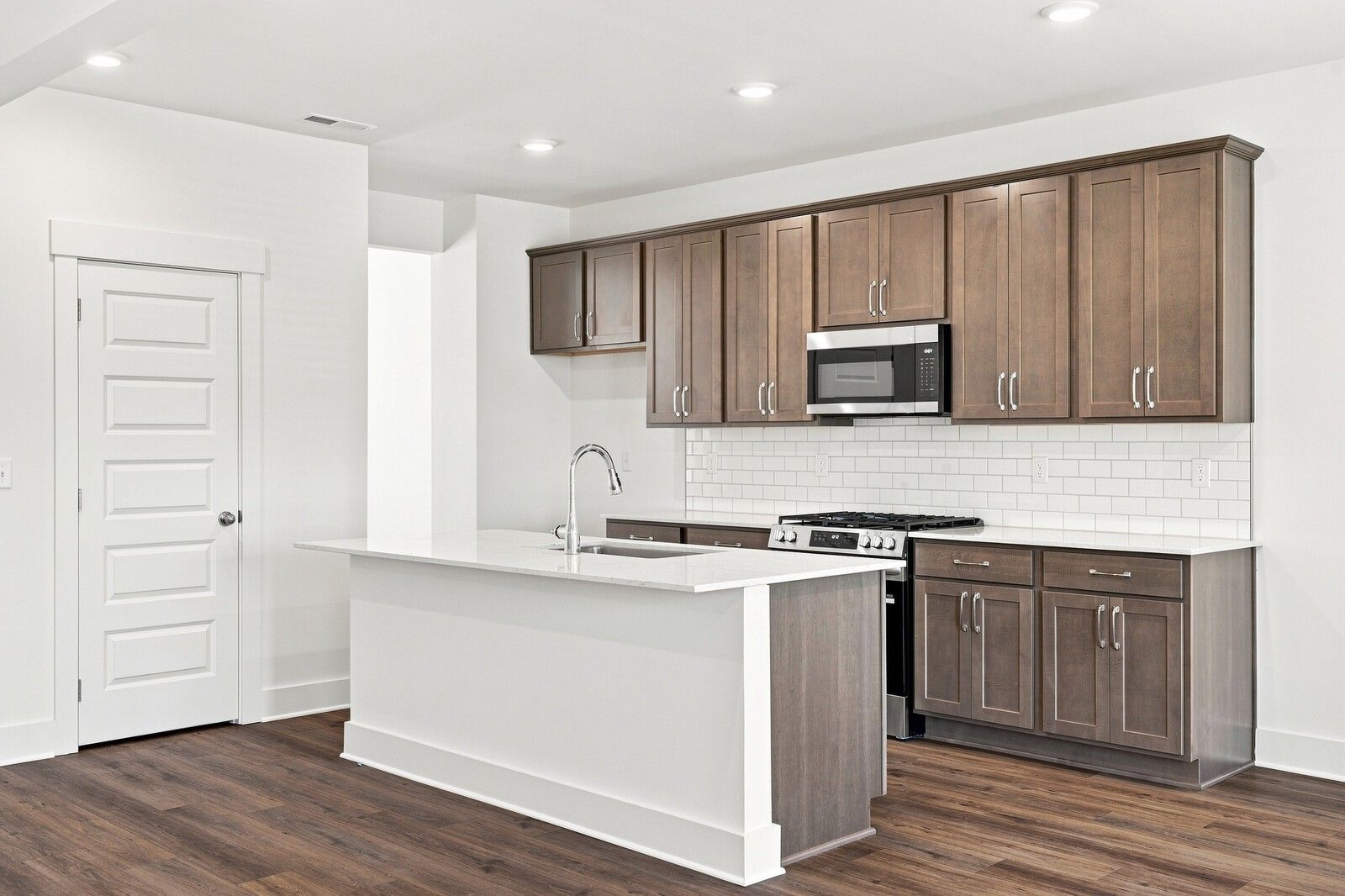 Kitchen island with white quartz countertop, stained cabinets, subway tile backsplash in Davidson Homes Willow C, Gallatin, TN