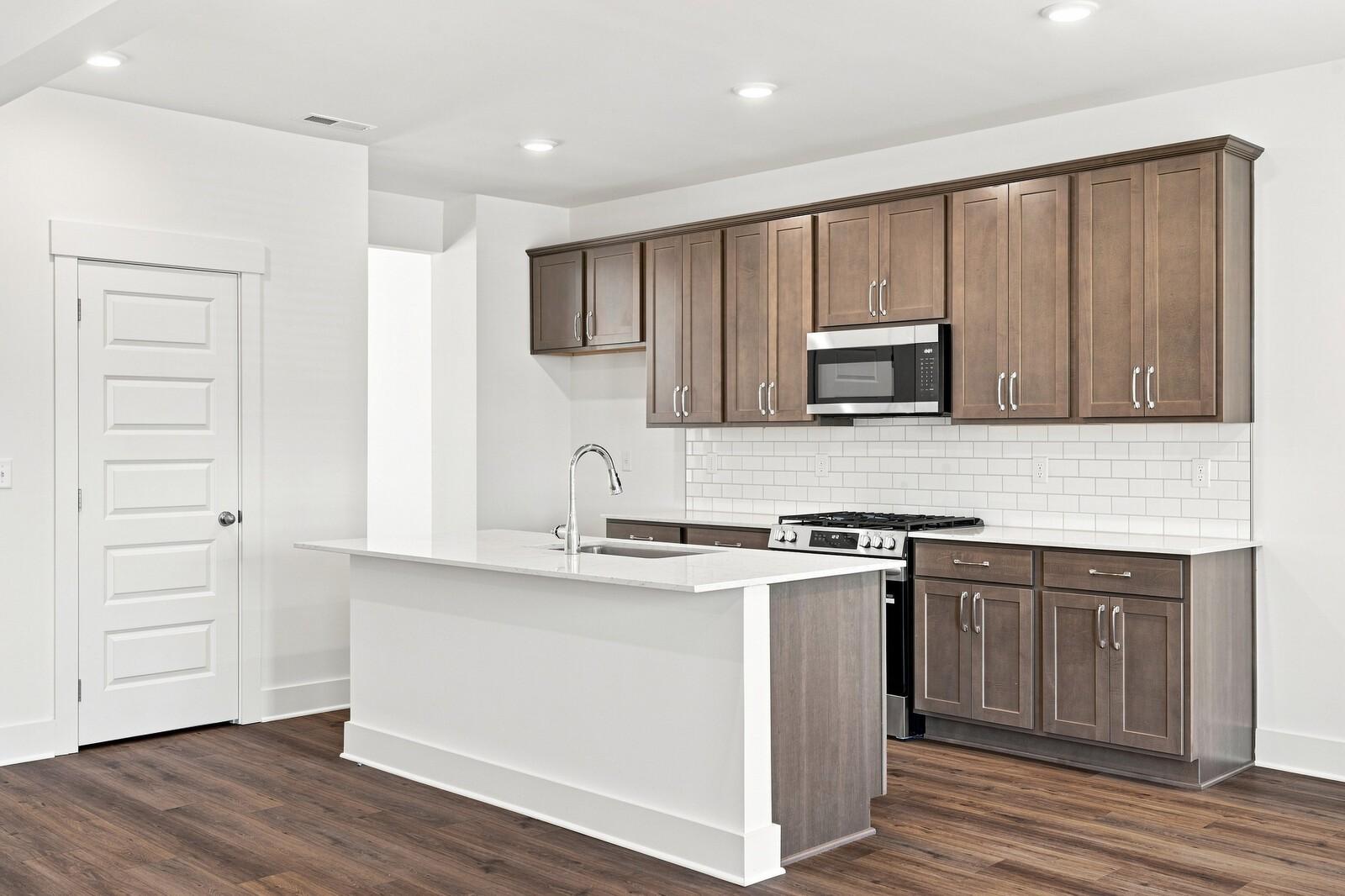 Kitchen island with white quartz countertop, stained cabinets, subway tile backsplash in Davidson Homes Willow C, Gallatin, TN