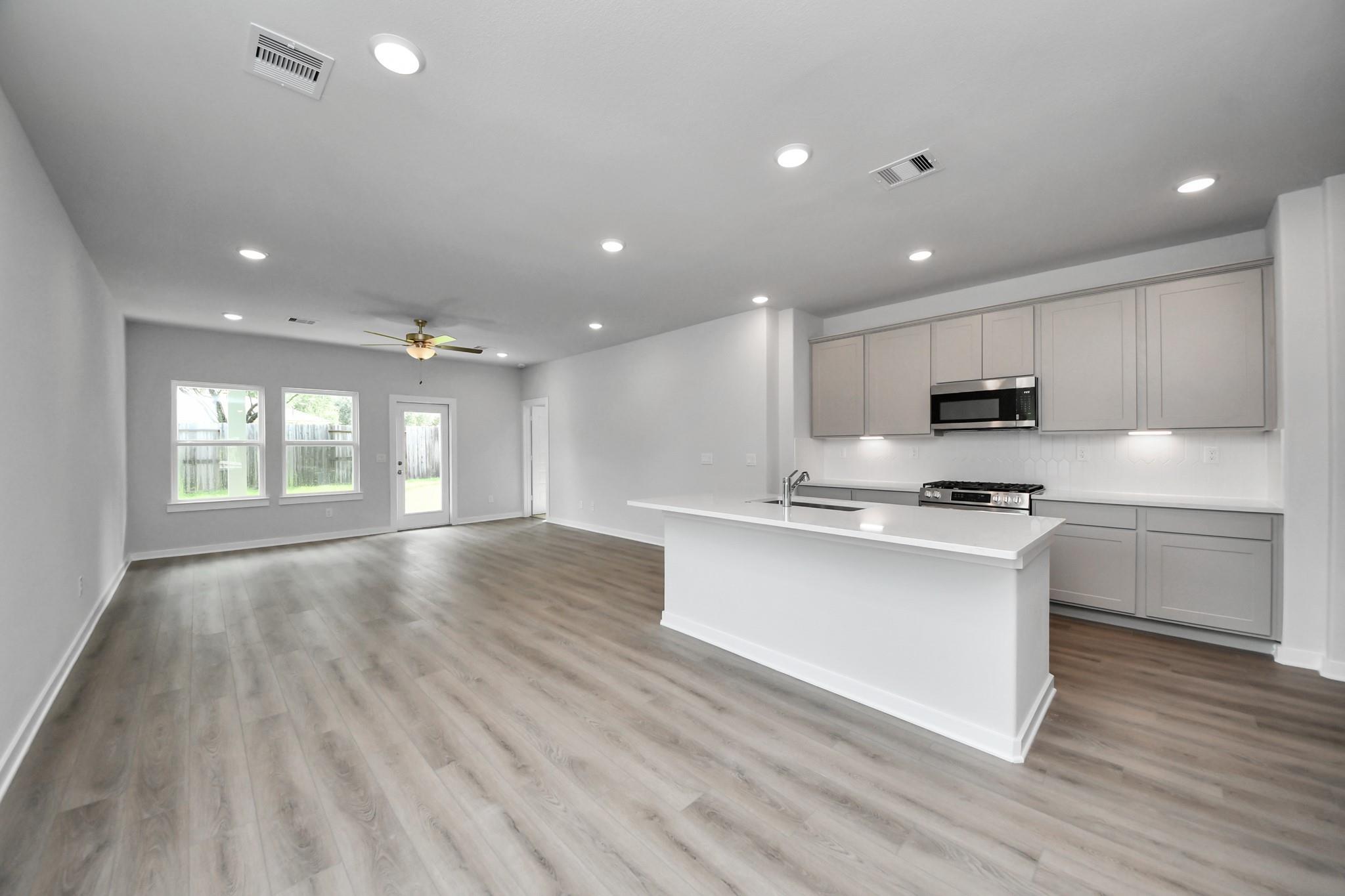 Open-concept kitchen with white island, gray shaker cabinets, and stainless appliances in Davidson Homes Blanco E plan, Magnolia TX