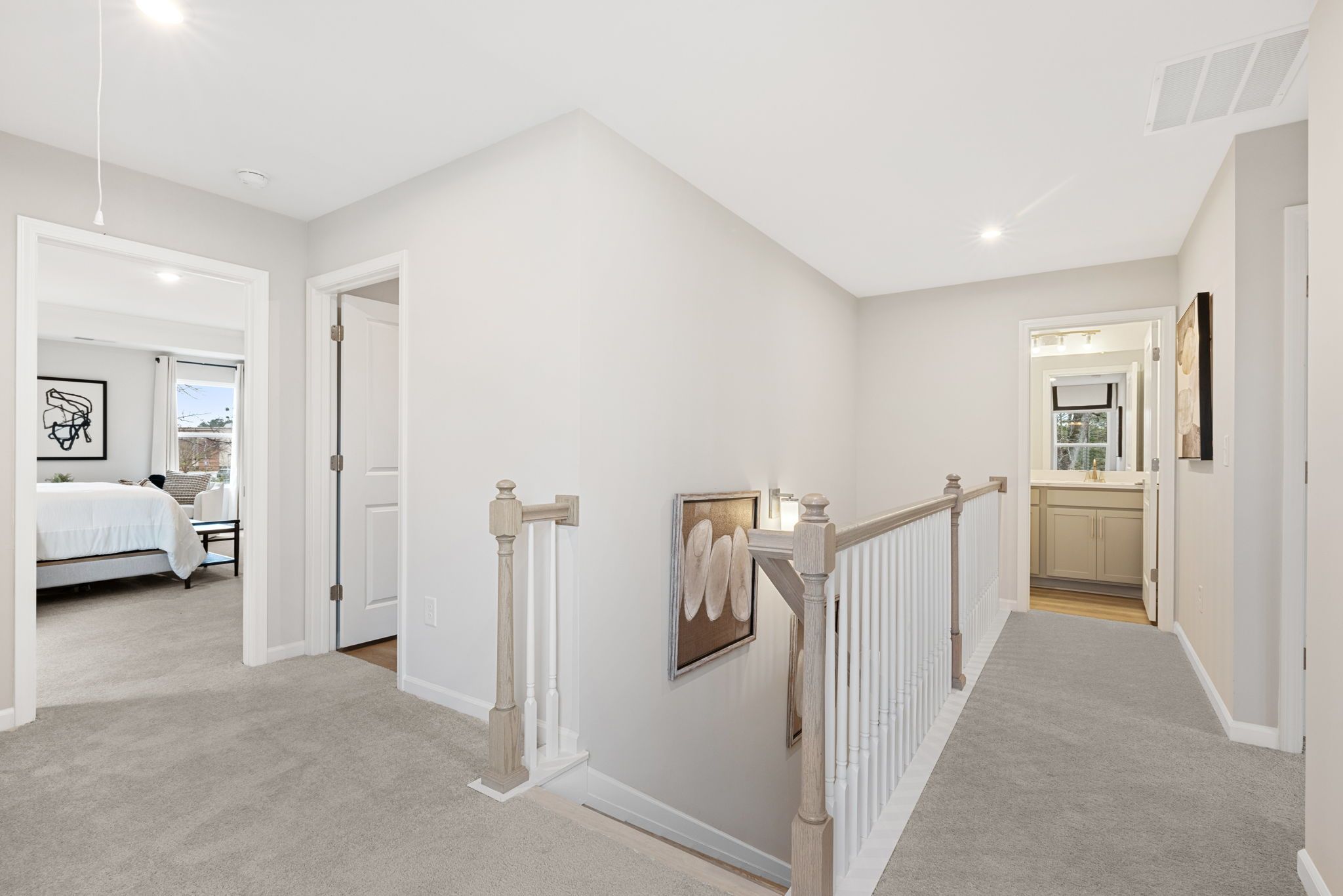 Spacious upstairs hallway in Lake Shore home by Davidson Homes, Winder GA, with white walls, gray carpet, staircase railing, bedroom, and bath