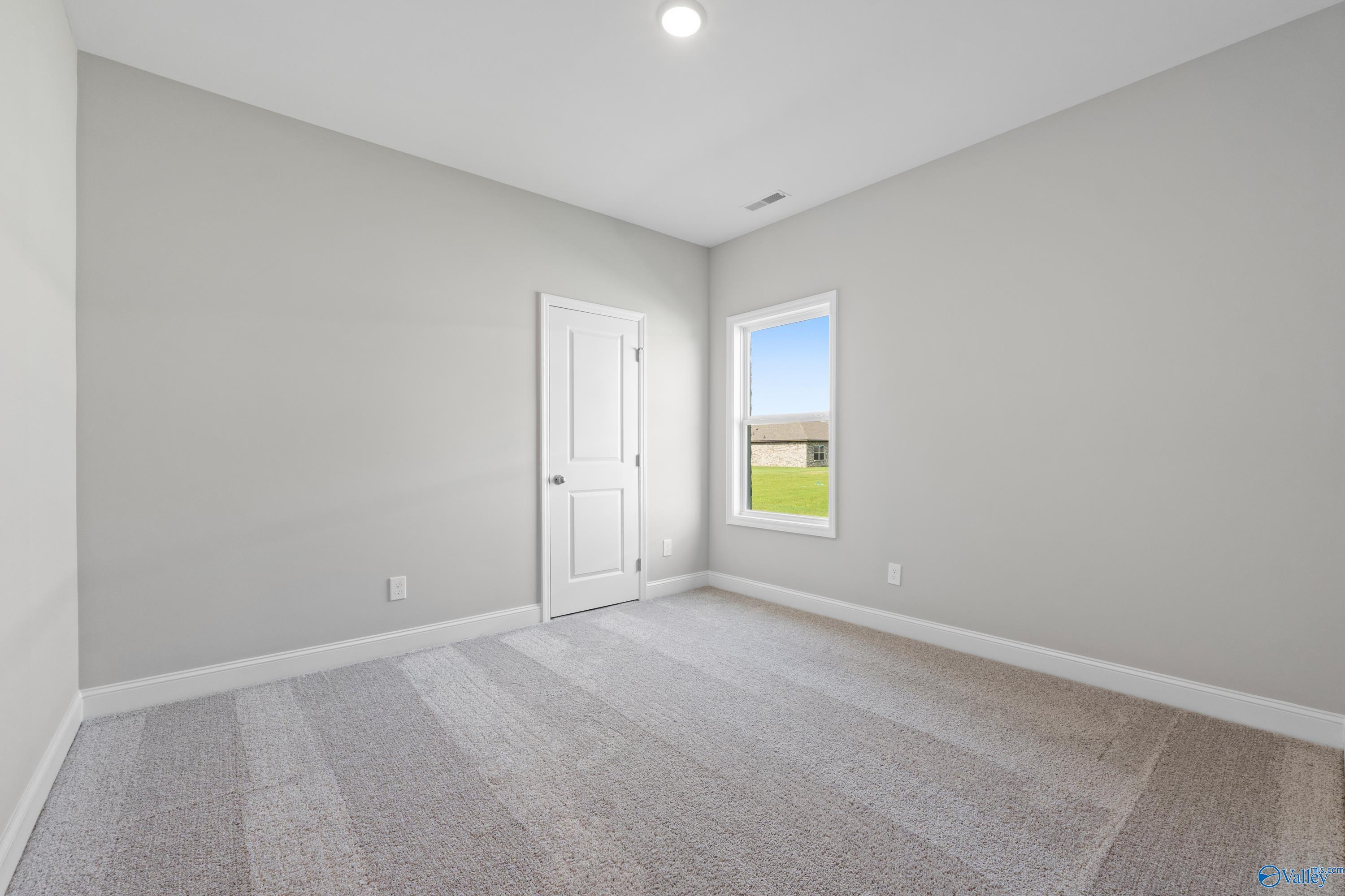 Neutral bedroom with gray walls, plush carpet, white door, and window overlooking green field in Davidson Homes The Everett B, Toney, AL