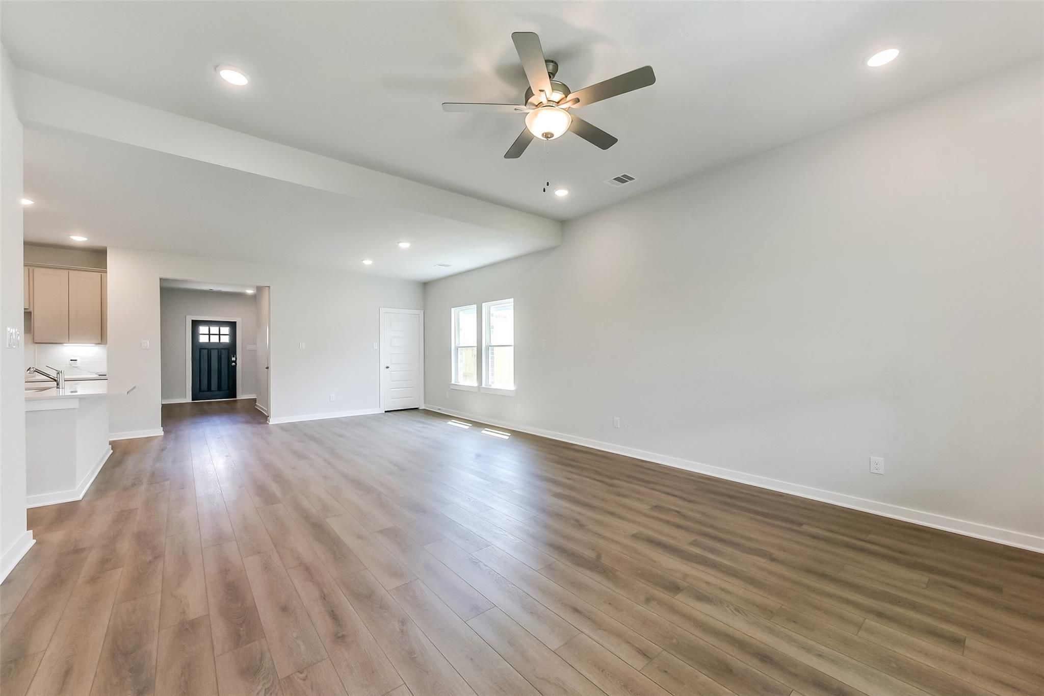 Spacious open living room with ceiling fan, hardwood floors, and adjacent kitchen in Davidson Homes The Tierra C, Dayton, Texas
