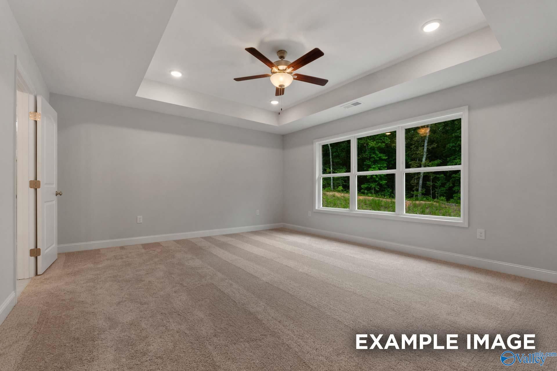 Spacious bedroom featuring ceiling fan, gray walls, beige carpet, and large windows with wooded view in Davidson Homes The Shelby C, Arab, Alabama
