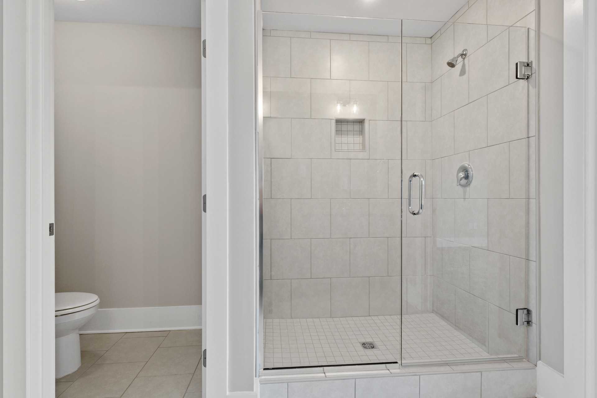 Spacious walk-in shower with frameless glass door and white subway tile in primary bathroom at Little Burwell Estates, Harvest Alabama by Davidson Homes
