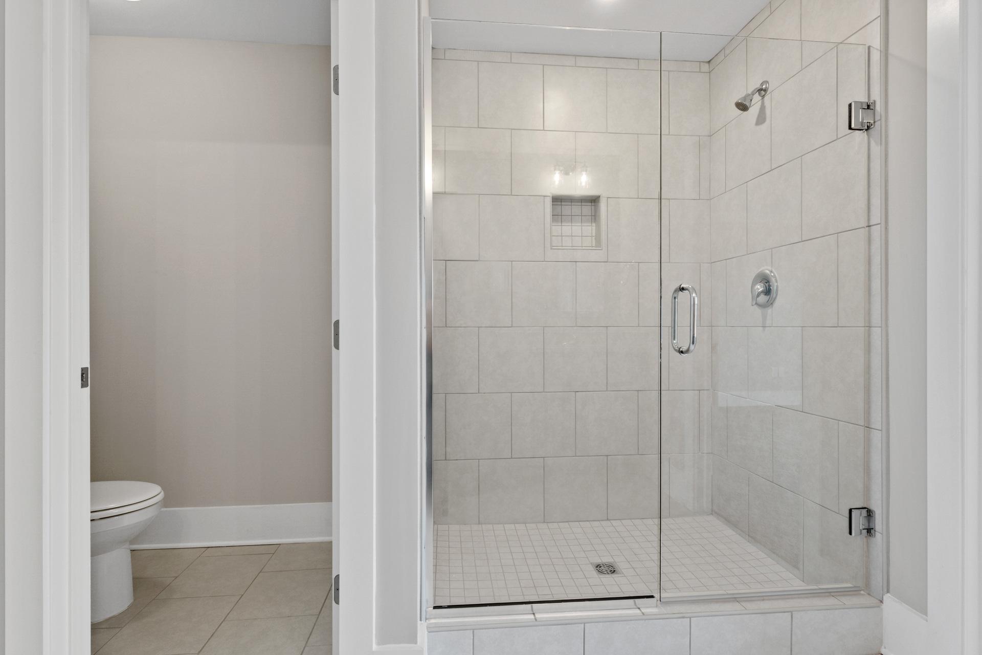 Spacious walk-in shower with frameless glass door and white subway tile in primary bathroom at Little Burwell Estates, Harvest Alabama by Davidson Homes
