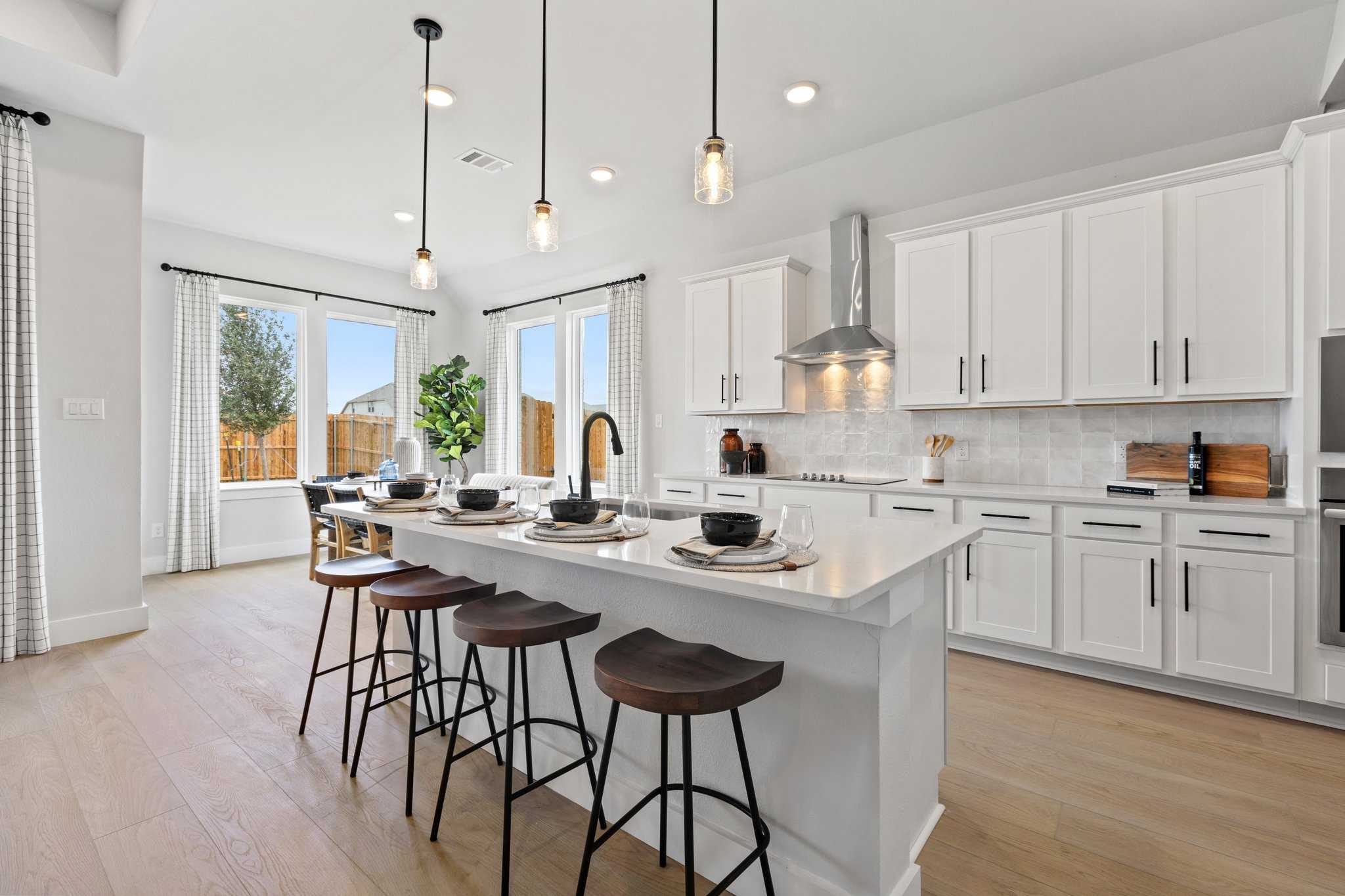 Spacious white kitchen with island bar stools, pendant lights, and stainless appliances in Davidson Homes Sequoia N, Josephine, Texas