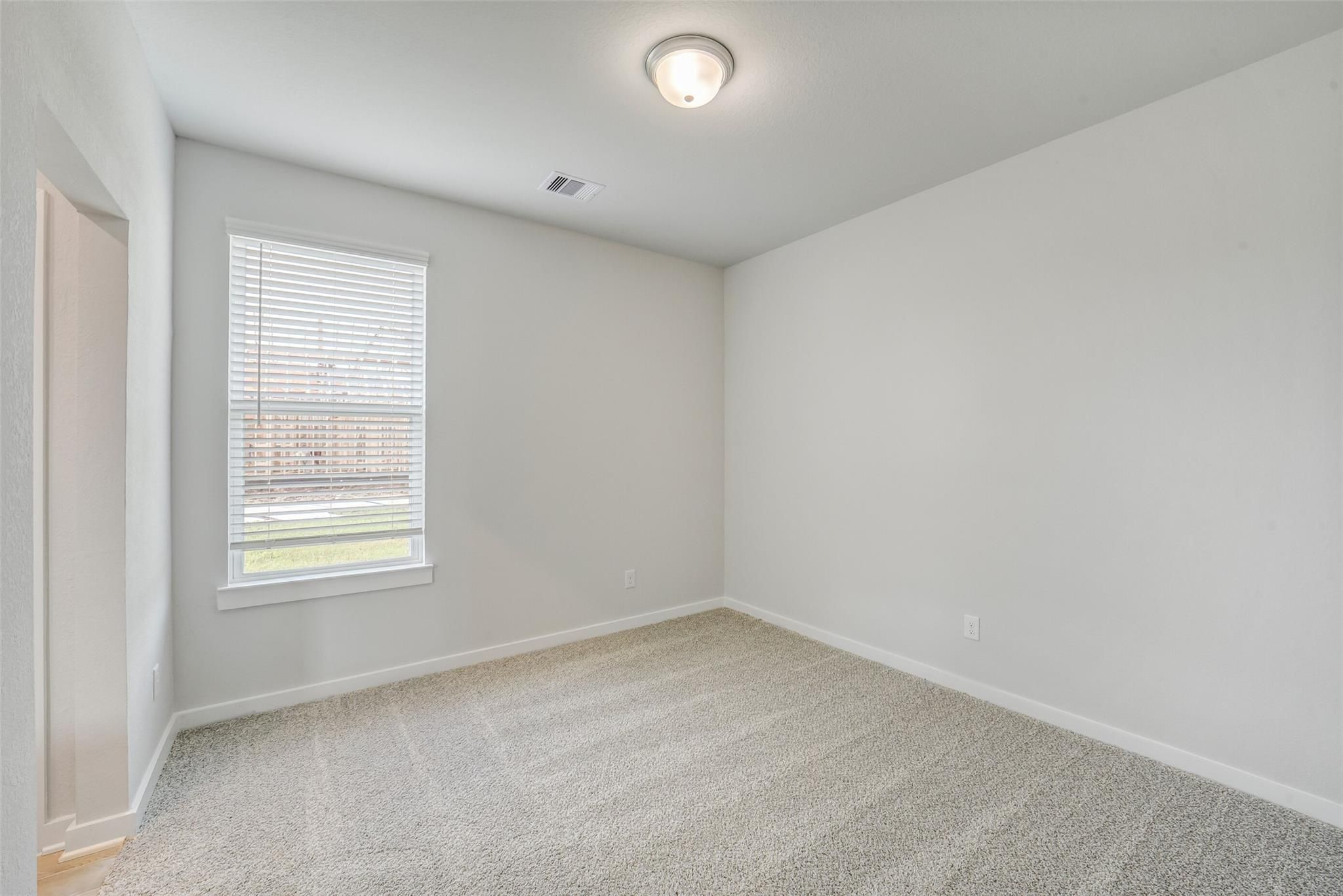 Bright empty bedroom with light gray walls, beige carpet, and window blinds overlooking lawn in Davidson Homes Acadia C, Magnolia TX