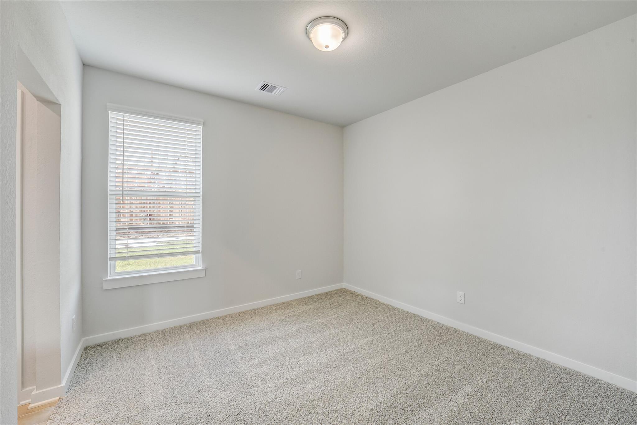 Bright empty bedroom with light gray walls, beige carpet, and window blinds overlooking lawn in Davidson Homes Acadia C, Magnolia TX