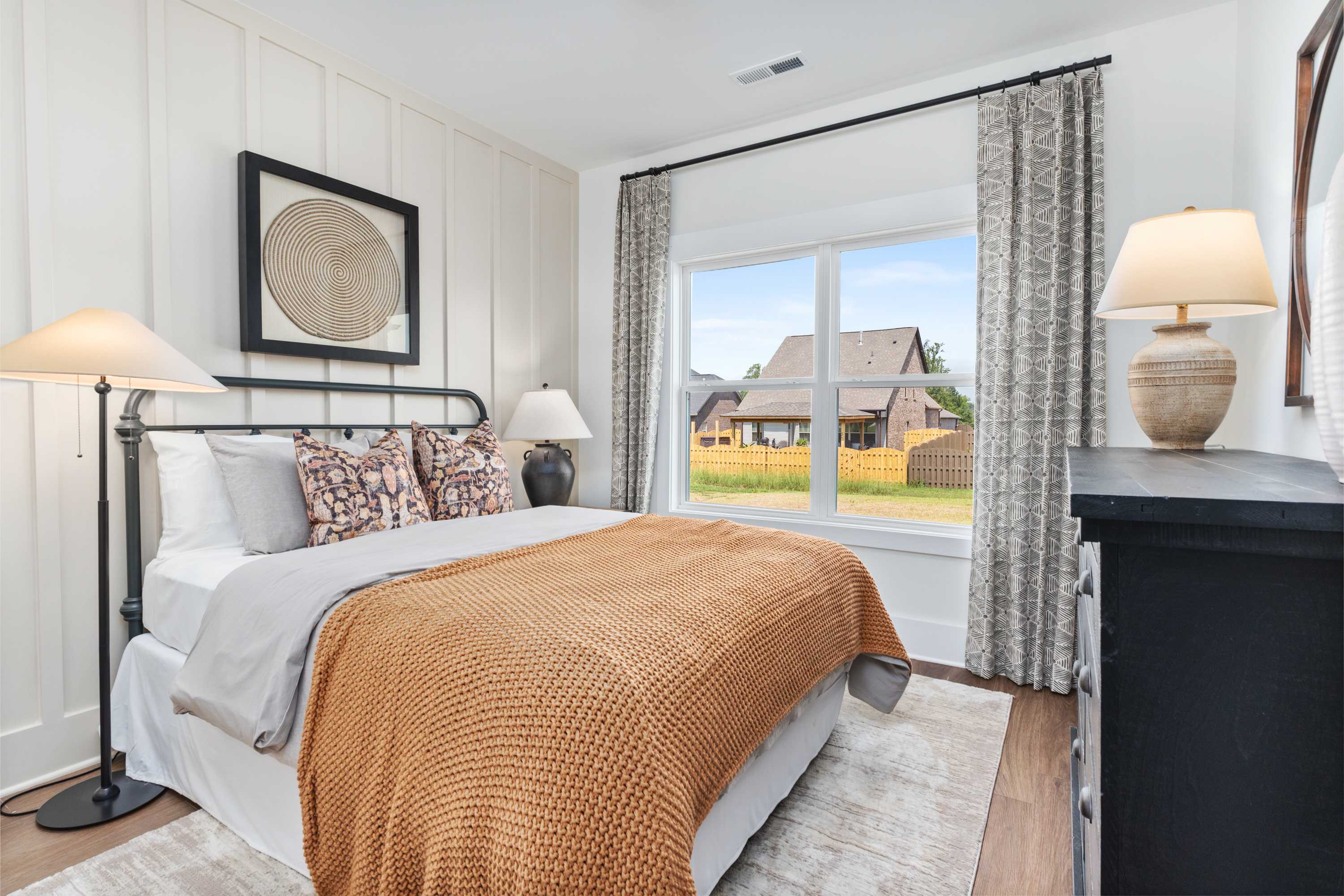 Spacious master bedroom in The Shelby A with white shiplap walls, king bed, orange throw, lamps, and backyard view