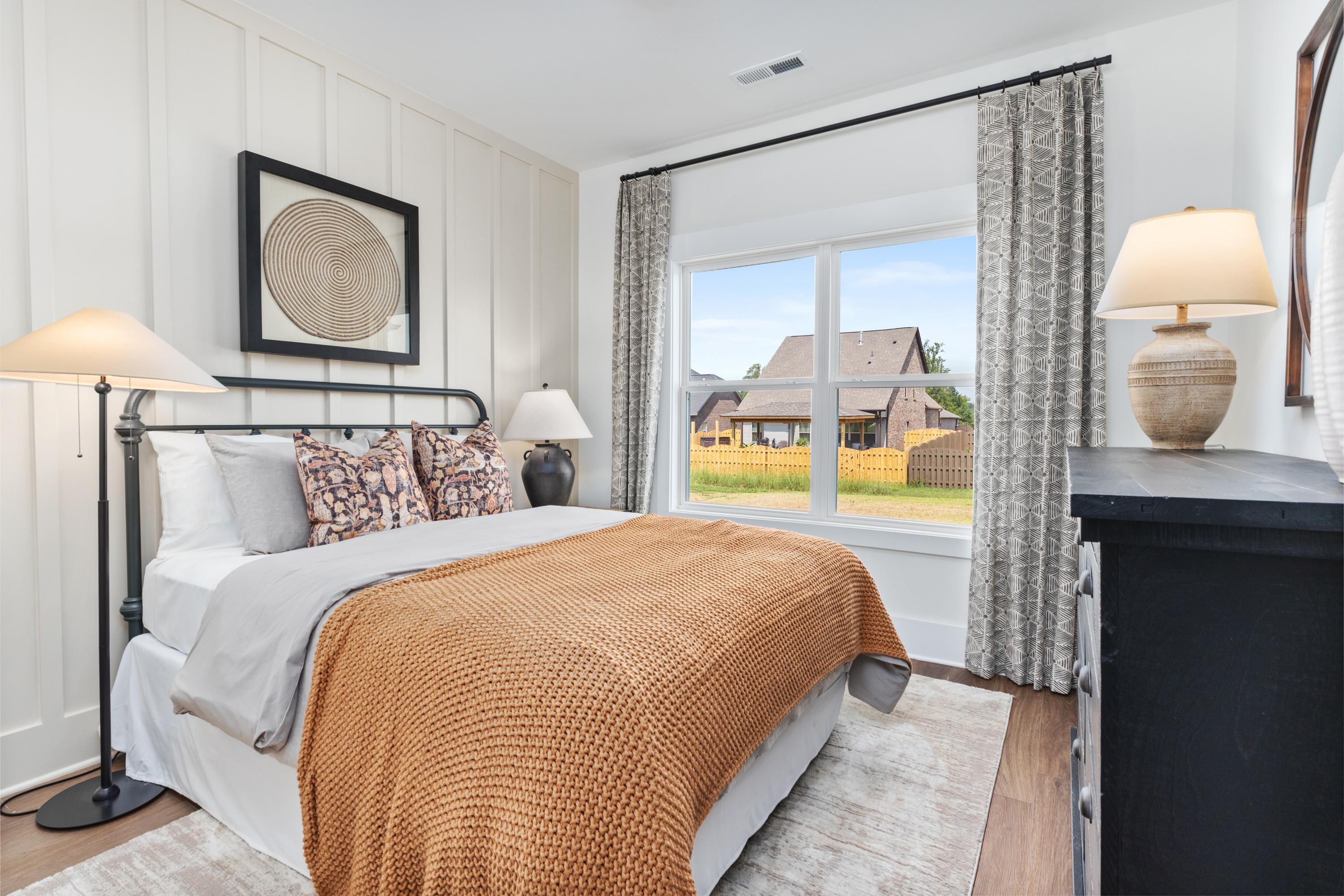 Spacious master bedroom in The Shelby A with white shiplap walls, king bed, orange throw, lamps, and backyard view
