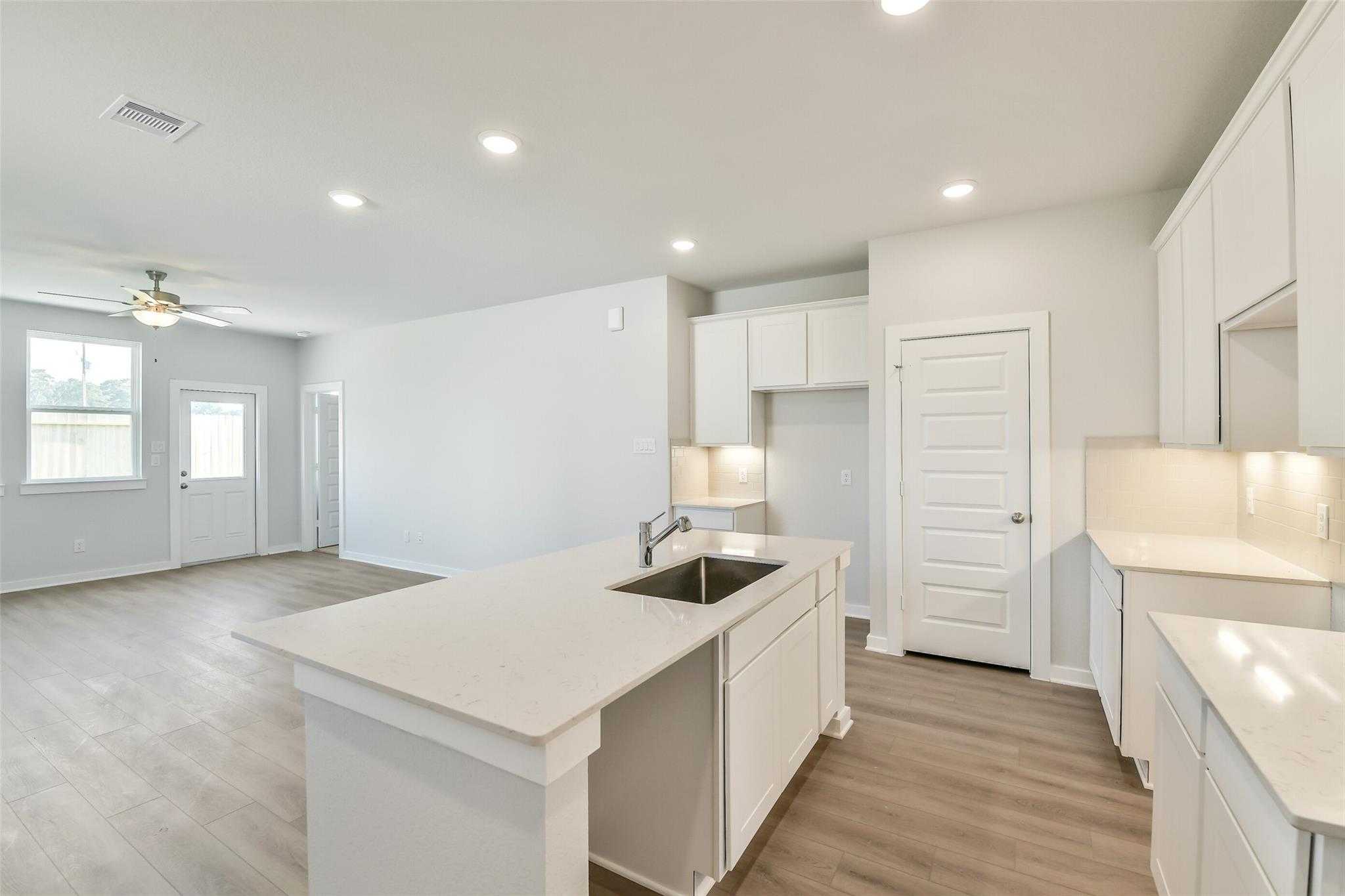 Modern white kitchen island with sink and cabinets in open-concept living area, The Colorado F 4-bedroom home by Davidson Homes, Cleveland Texas