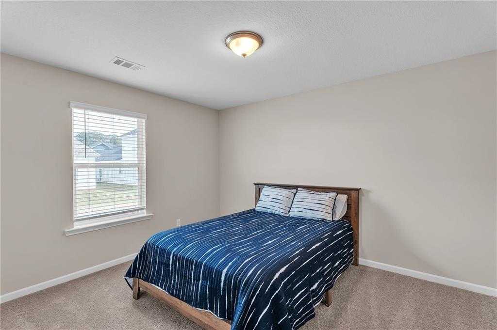 Cozy bedroom with blue shibori comforter on wooden bed, beige walls, and window view in Davidson Homes The Bartlett, Phenix City, AL