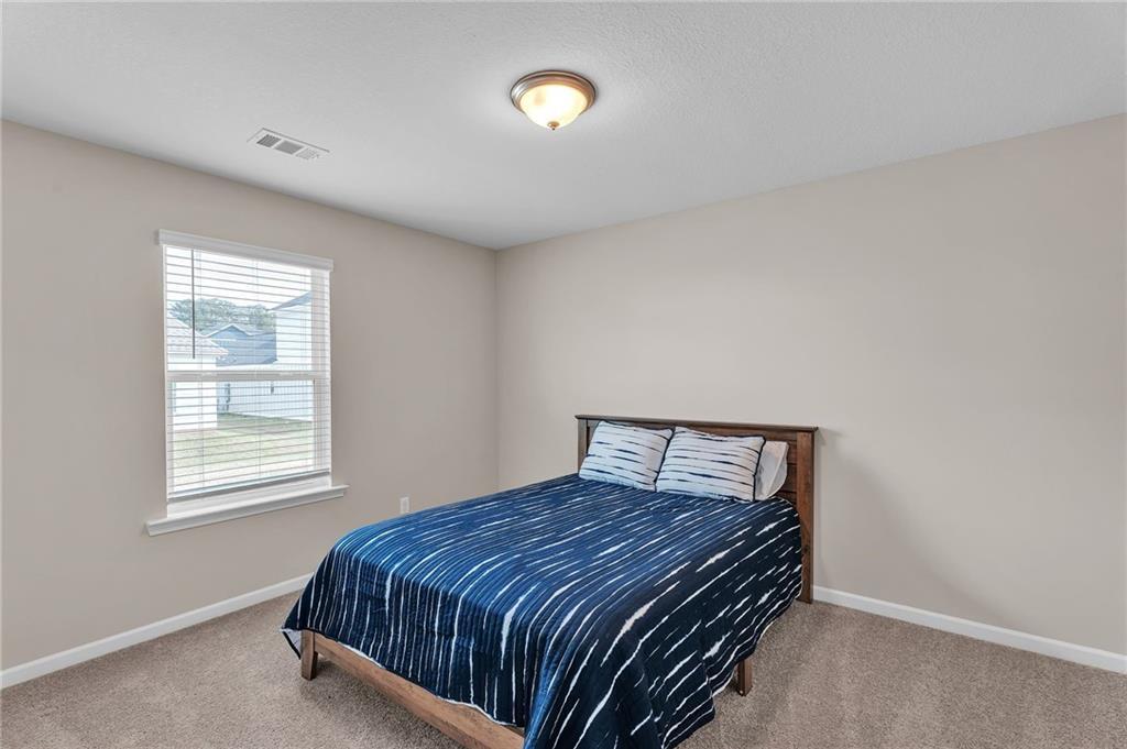 Cozy secondary bedroom with wooden bed frame, blue tie-dye comforter, beige walls and window blinds in Davidson Homes The Bartlett, Phenix City, Alabama