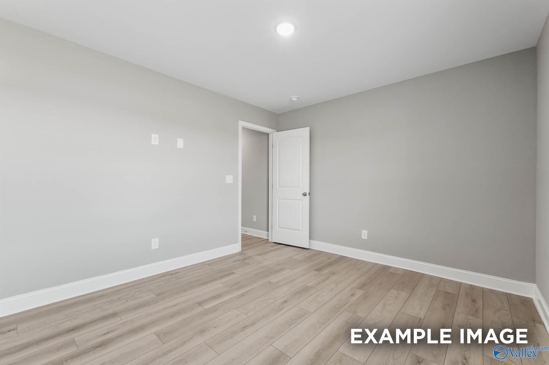 Empty bedroom featuring gray walls, light wood laminate floors, and open white door in Davidson Homes The Everett B, Toney, Alabama