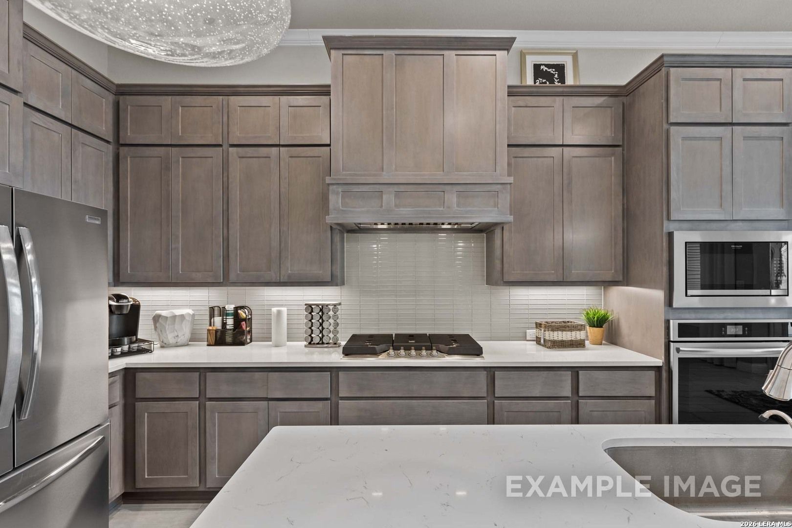 Modern kitchen with grey cabinetry, quartz countertops, and stainless steel appliances in The Garner C, Castroville, Texas.