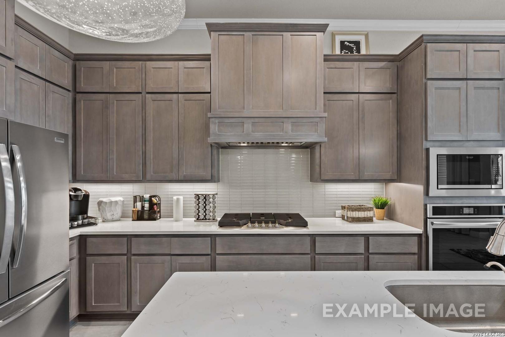 Modern kitchen with grey cabinetry, quartz countertops, and stainless steel appliances in The Garner C, Castroville, Texas.