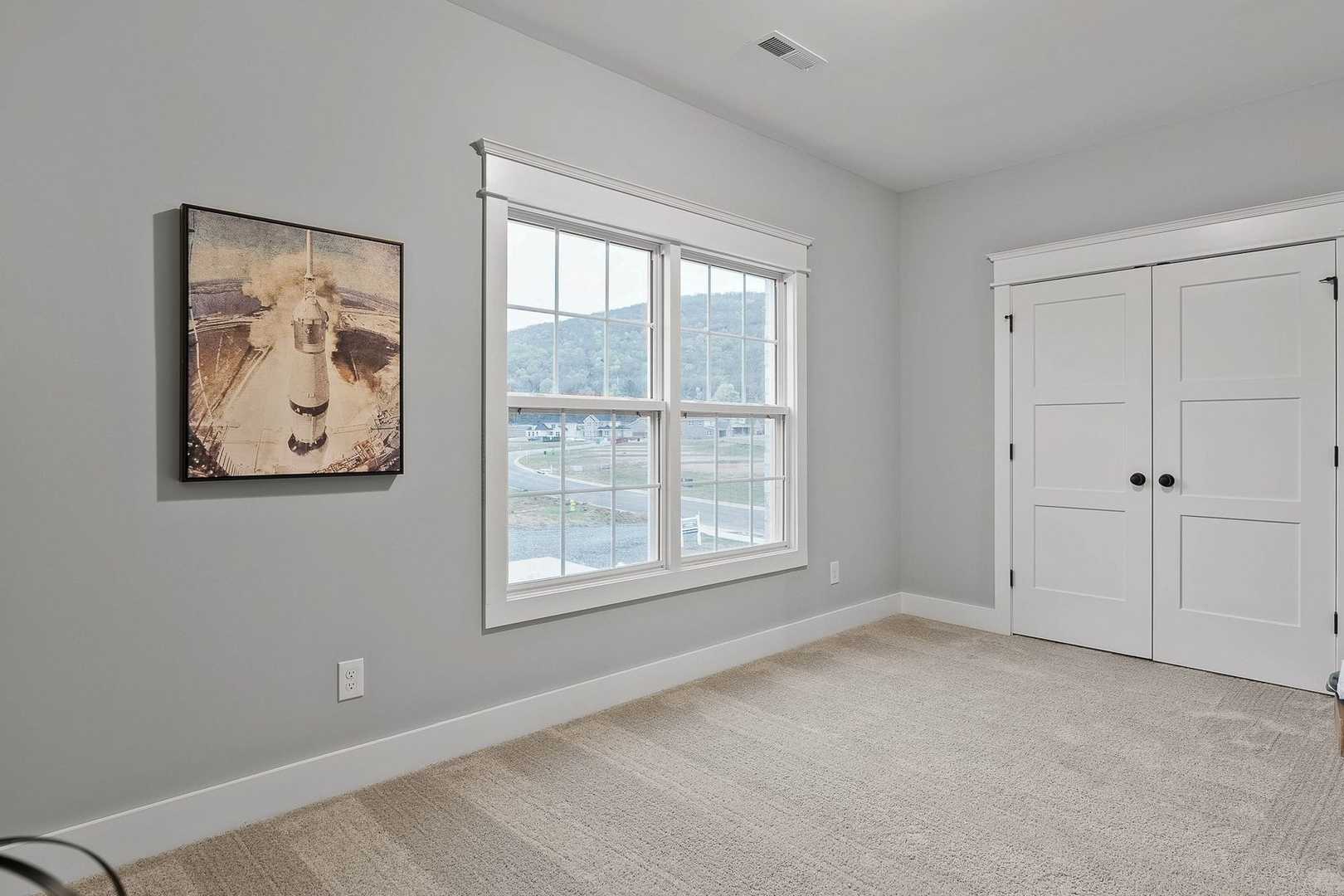 Spacious secondary bedroom in The Oxford home with light gray walls, large window view, double doors, and neutral carpet