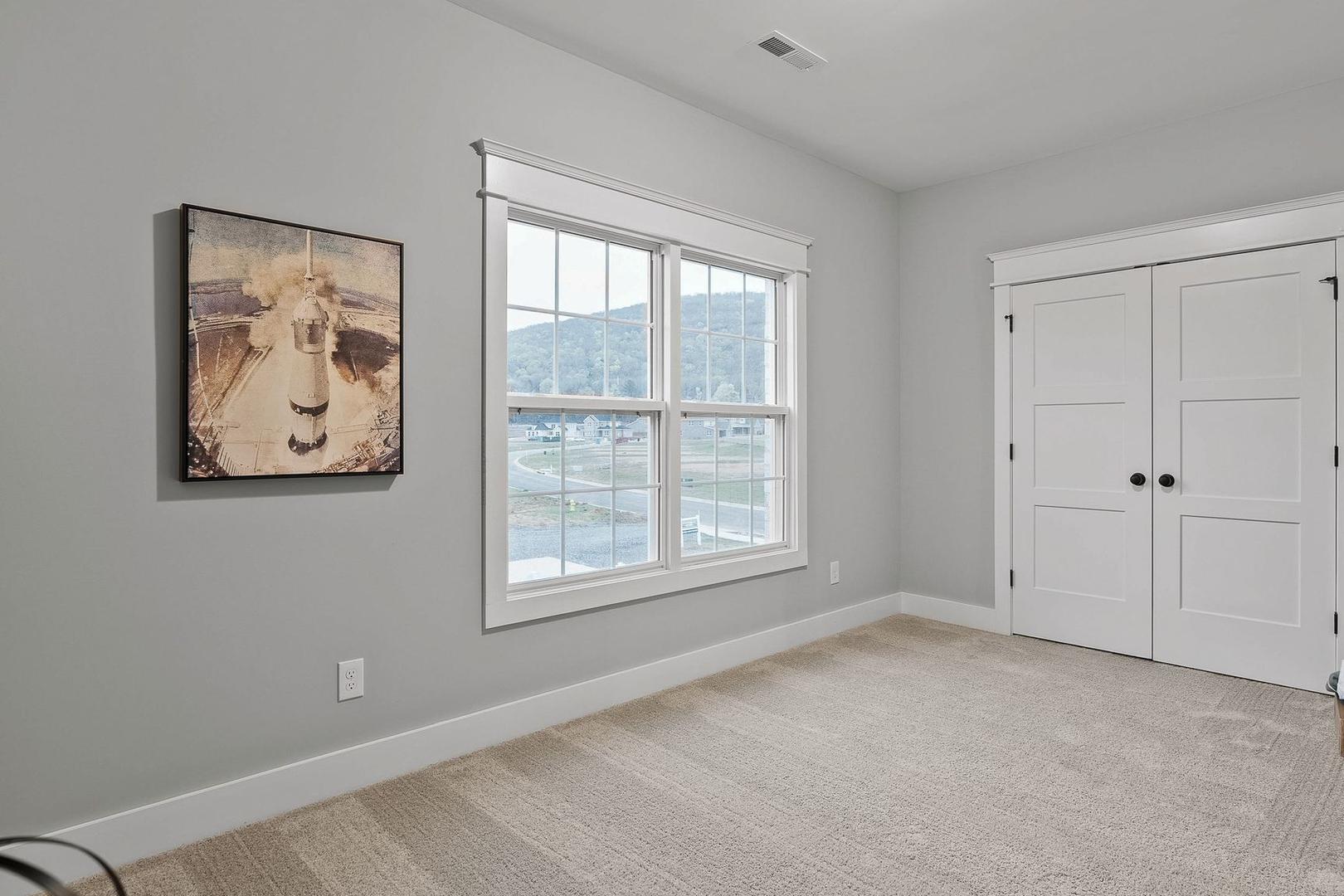 Spacious secondary bedroom in The Oxford home with light gray walls, large window view, double doors, and neutral carpet