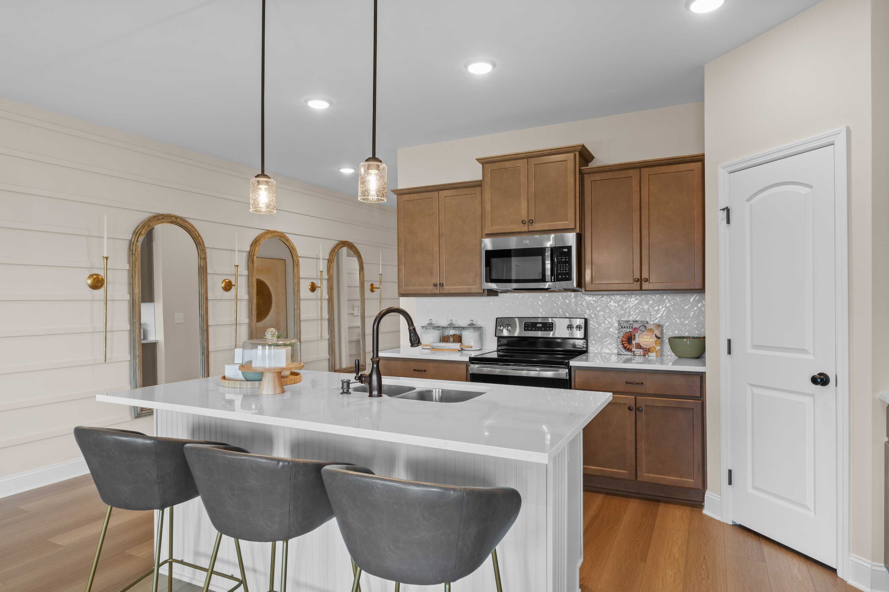 Modern kitchen in The Daphne F showcasing white quartz island, shaker wood cabinets, stainless appliances, and arched mirrors